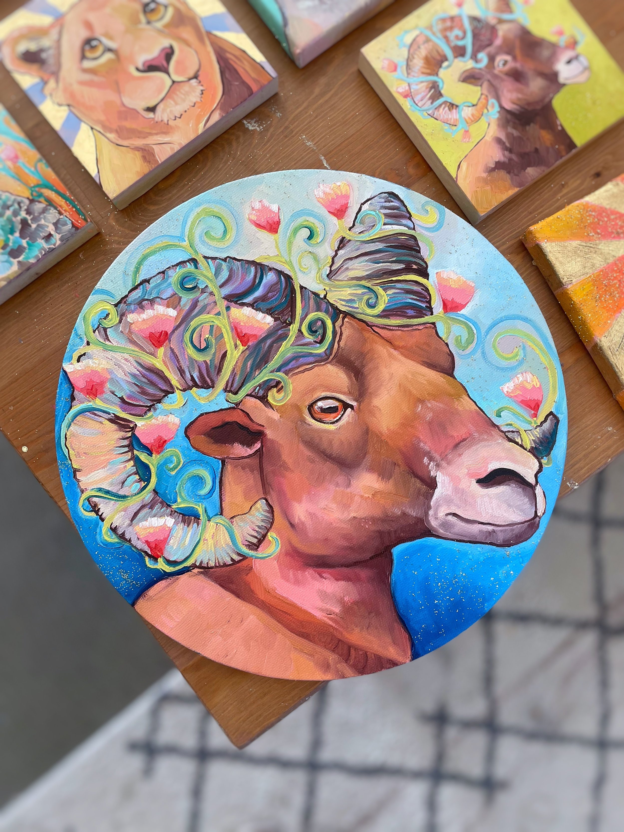 A round painting of a bighorn sheep with flowers around its horns