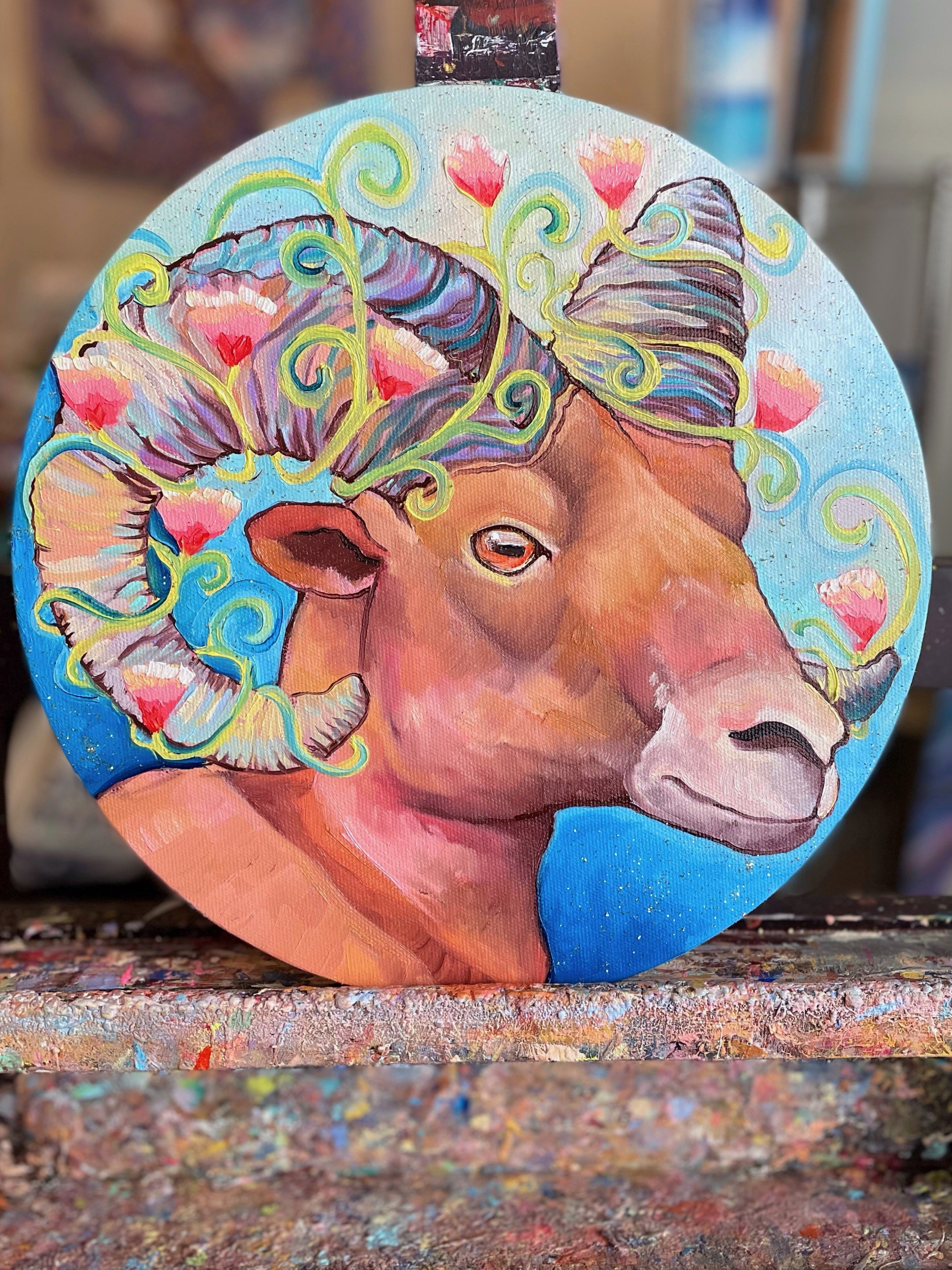 A round painting of a bighorn sheep with flowers around its horns