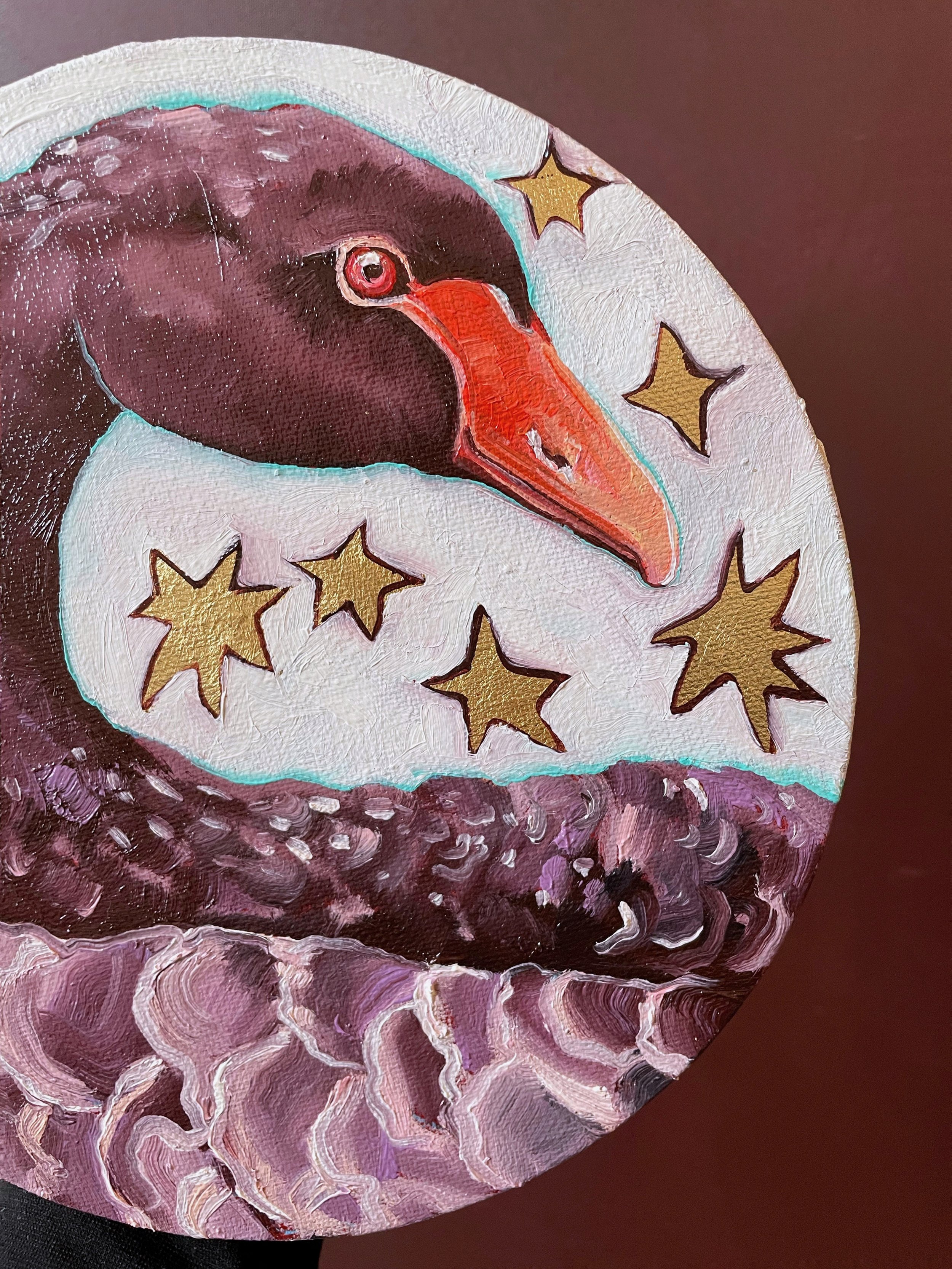 a round painting of a black swan surrounded by gold leaf stars
