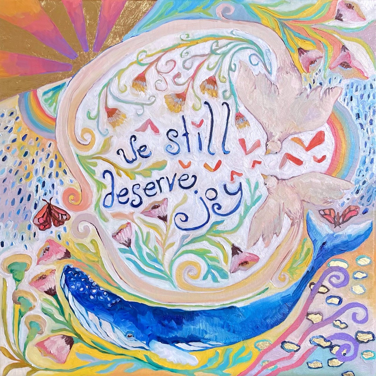 a colorful painting with a bird, flowers, a whale, and rainbows. the words 'we still deserve joy' are painted in the center.