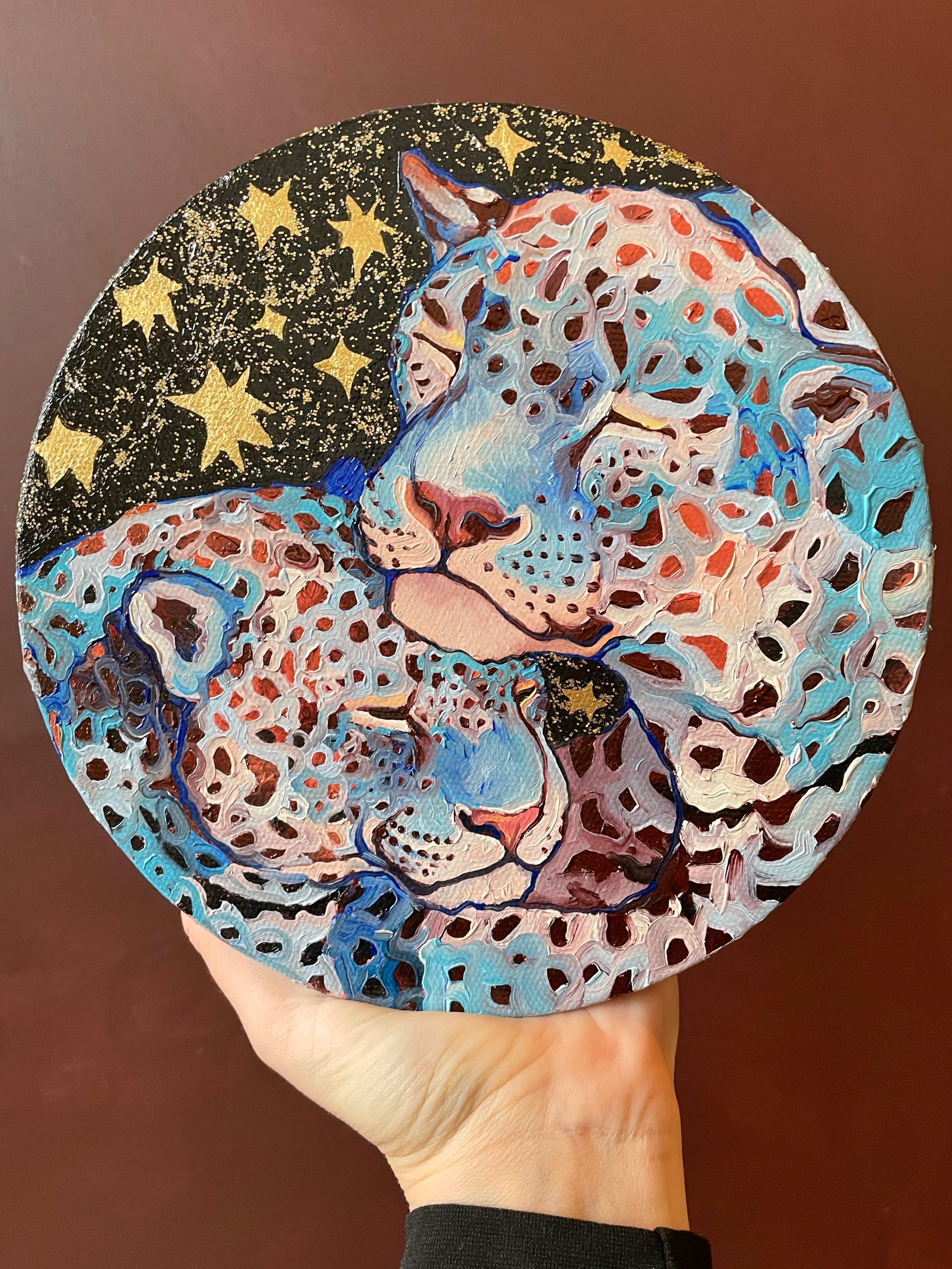 a round painting of two blue leopards nuzzling and sleeping under a black sky with golden stars and glitter.