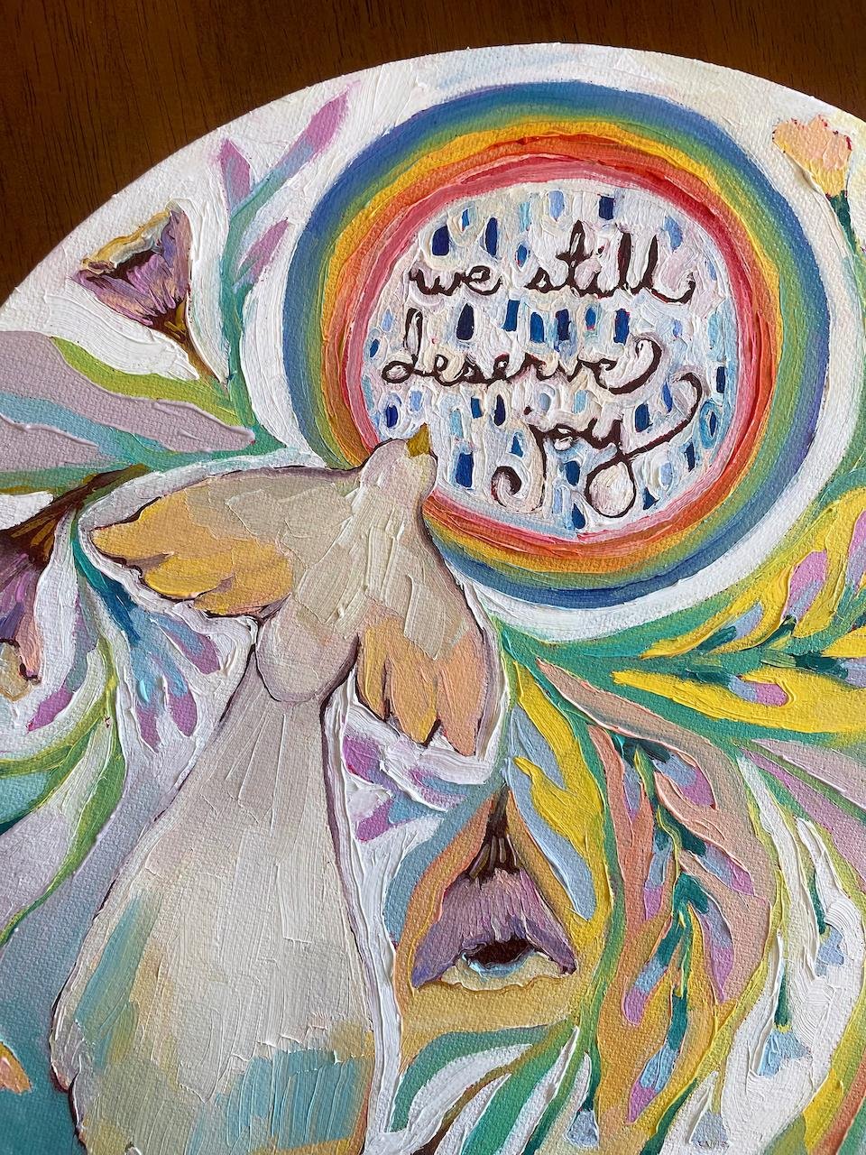 a close up on the painting showing a bird and the words we still deserve joy