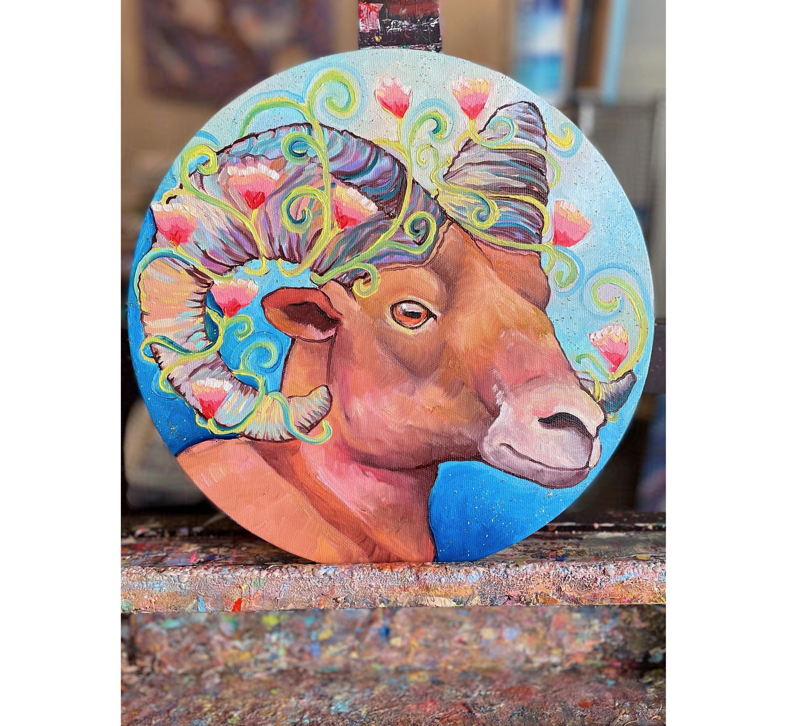 A round painting of a bighorn sheep with flowers around its horns