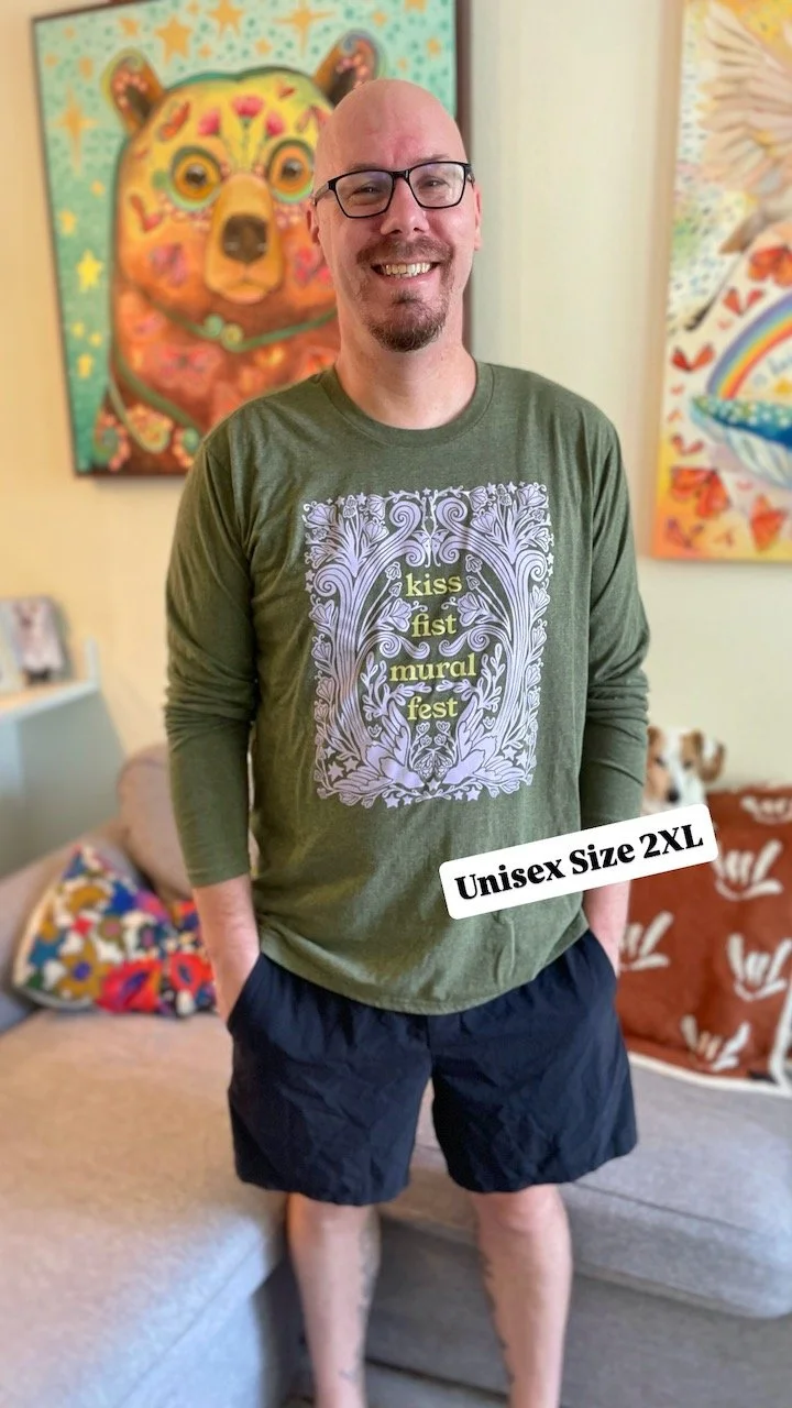 bobby, a white man with black framed glasses, smiles at camera showing the front of the shirt