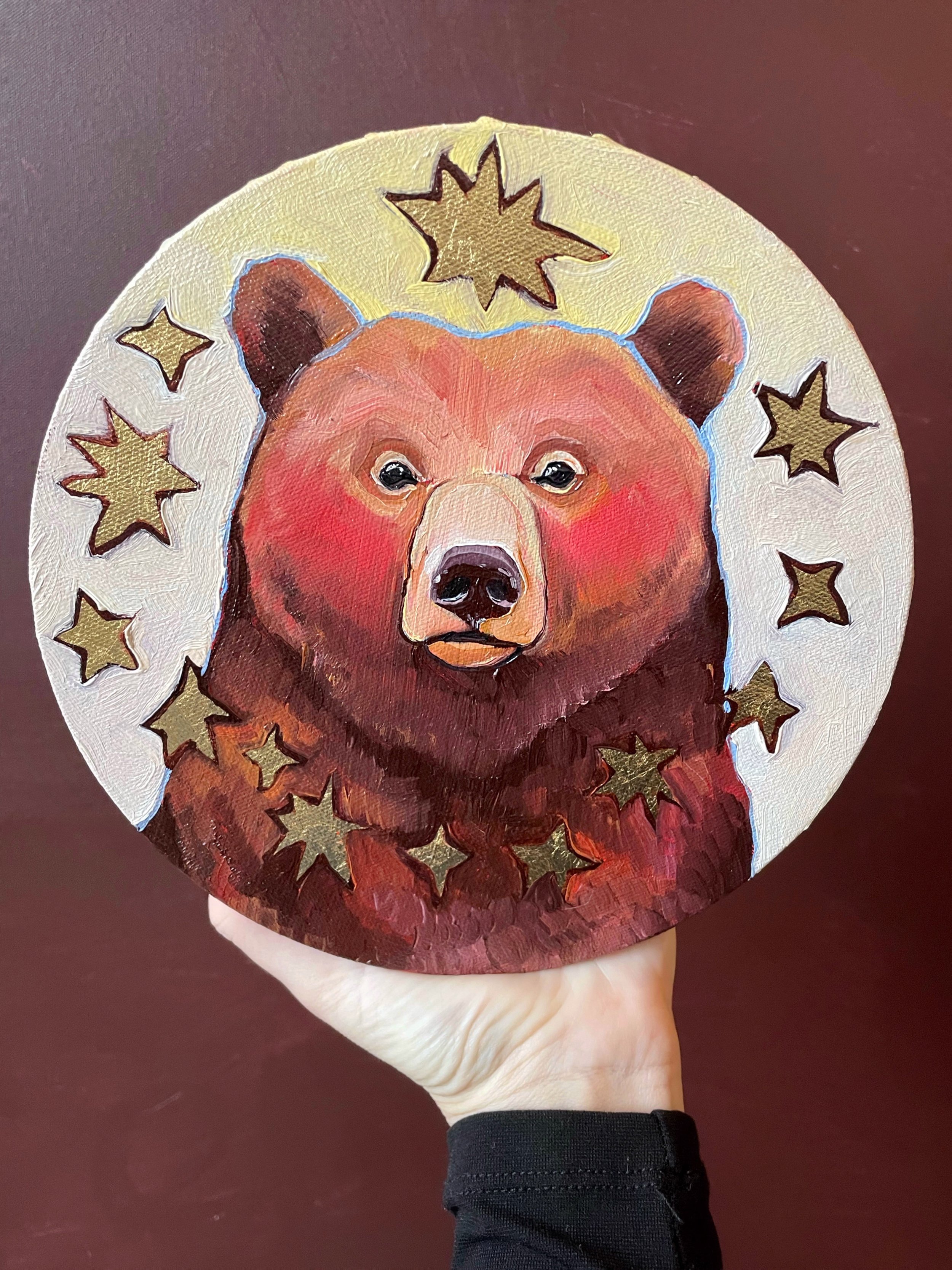 a round painting of a brown bear surrounded by golden stars