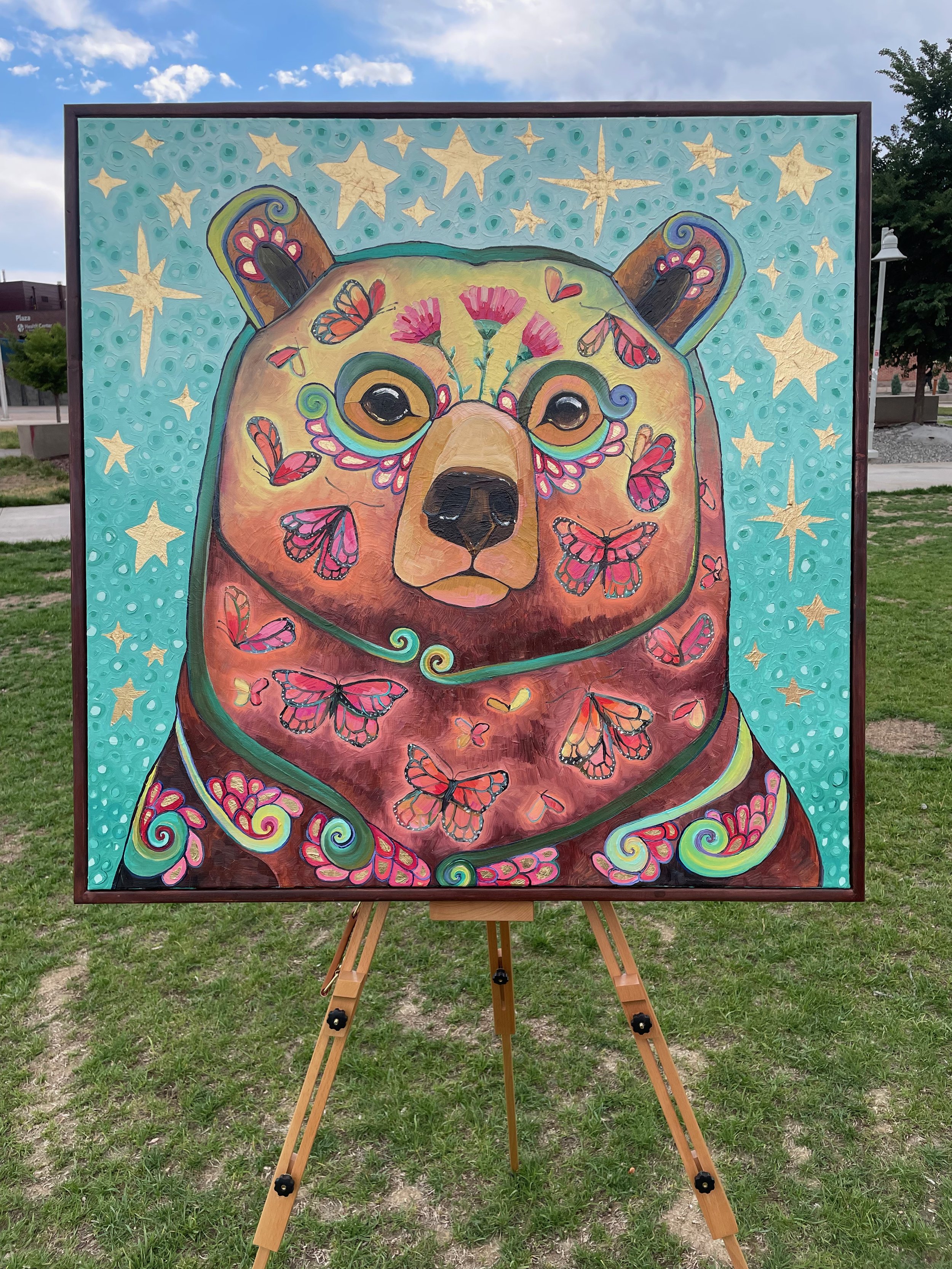 the framed butterfly bear painting on an easel outdoors