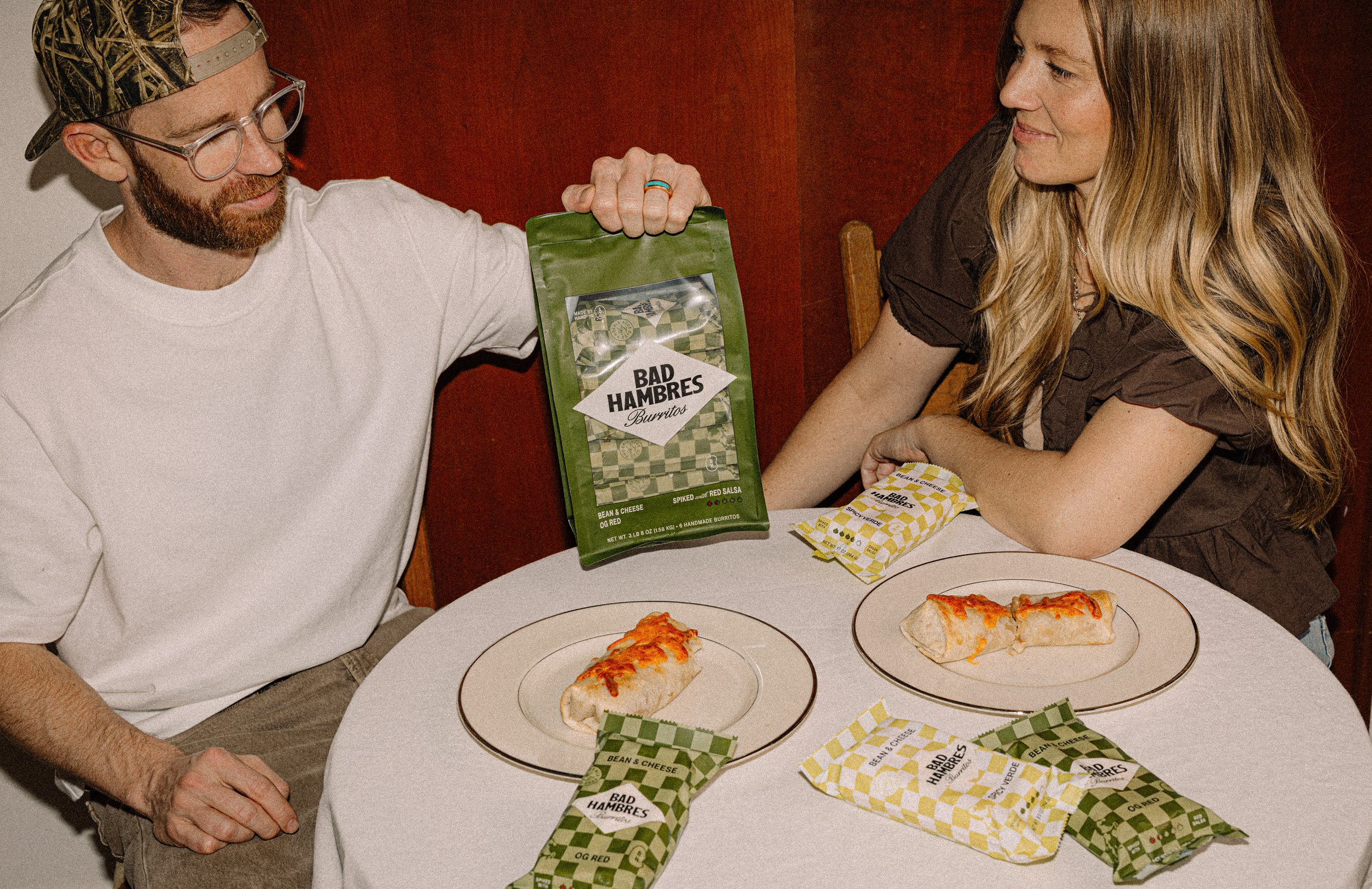 Bad Hambres owners Hank and Sam showing branded packaging set with burritos at table