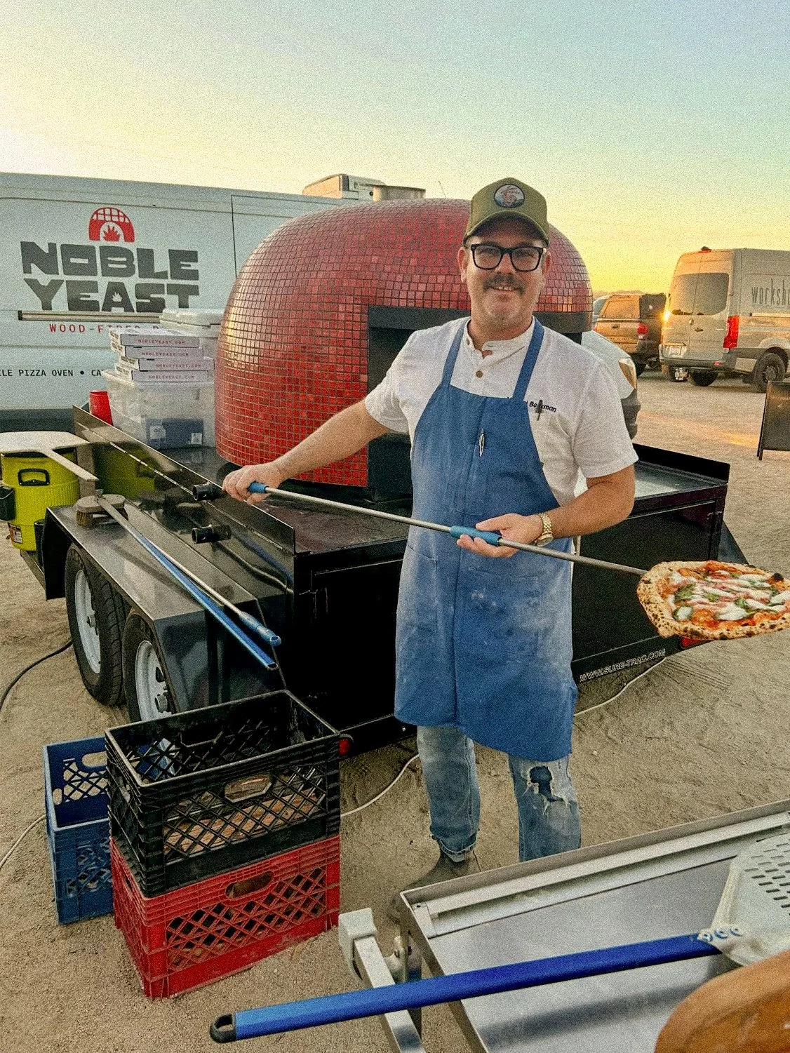 Chef Michael of Noble Yeast presenting wood-fired Neapolitan pizza outdoors branded logo signage on van in background