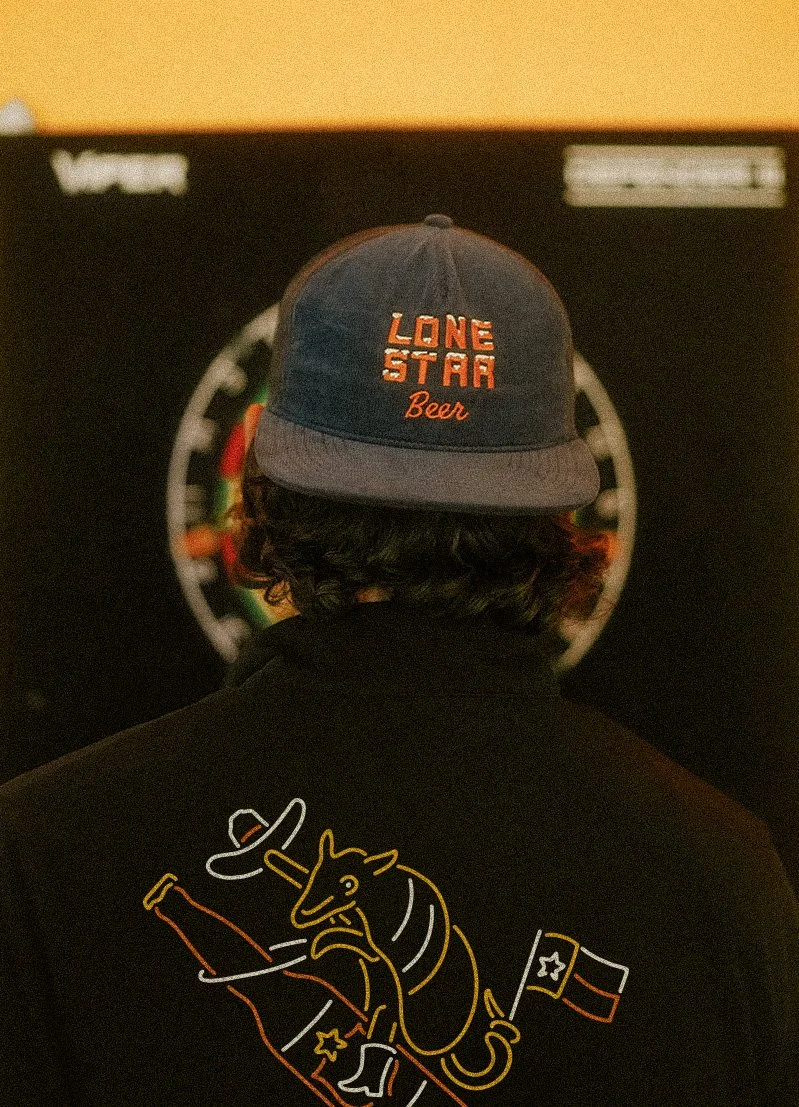 Lone Star Beer merch collection with ice letter embroidered hat and vintage neon sign bucking armadillo shirt design detail in dive bar setting