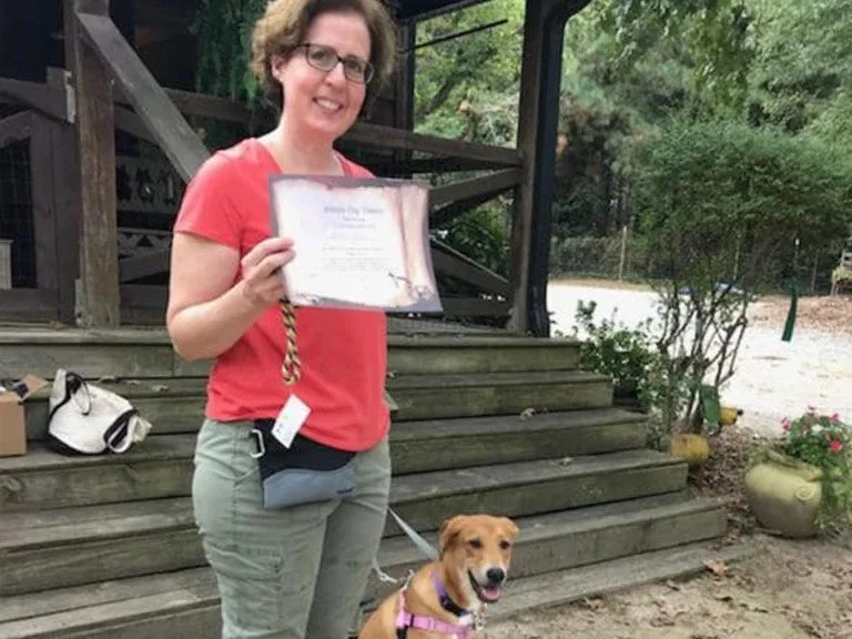Woman standing with her dog and showing certificate from puppy training class.