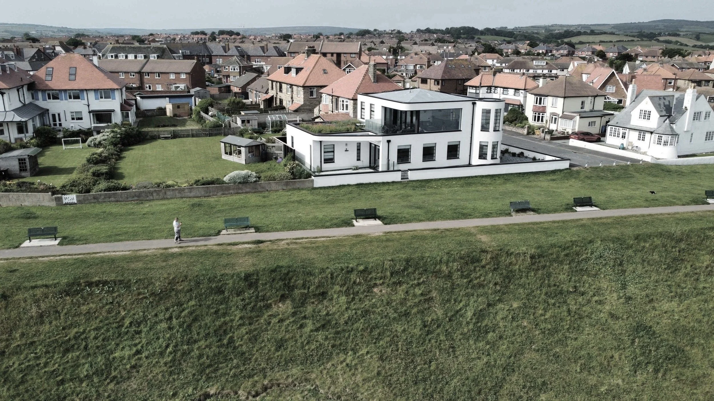 Drone view of the award-winning Poet's View in Whitby. A striking Art Deco house perched on a clifftop in Whitby, surrounded by a low white wall and gardens laid to grass.