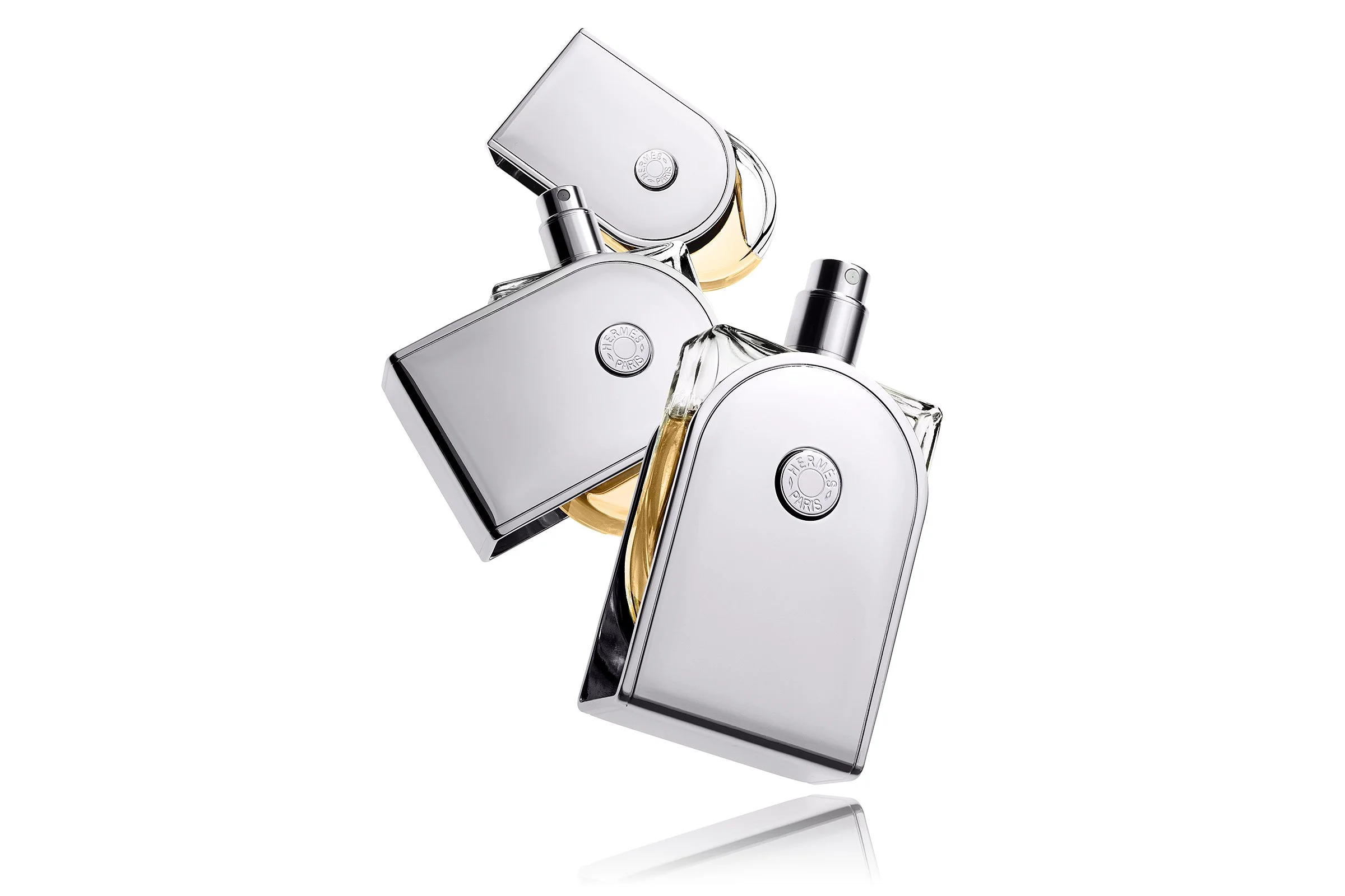 Three bottles of perfume with sleek, reflective silver and transparent glass design. Photography by Kenneth Foo.