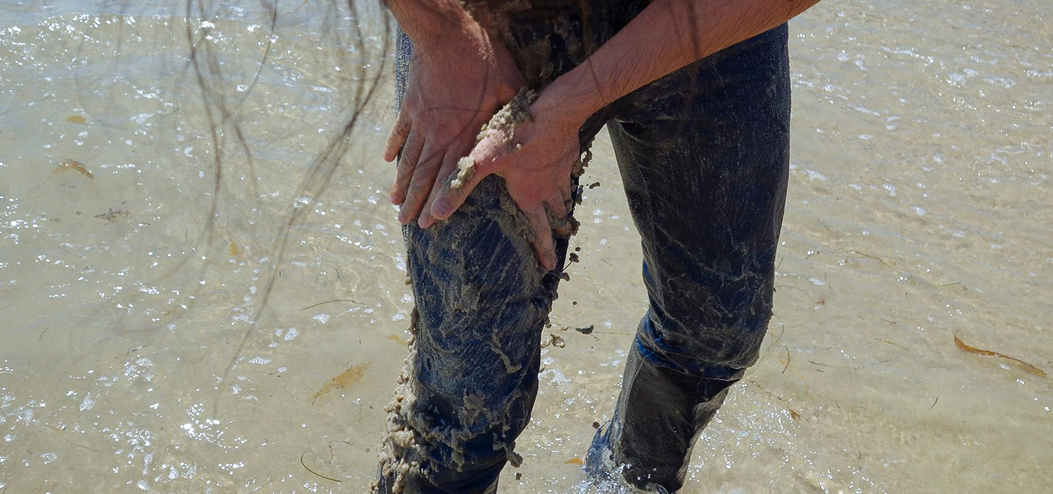 Man in the ocean rubbing sand onto his jeans