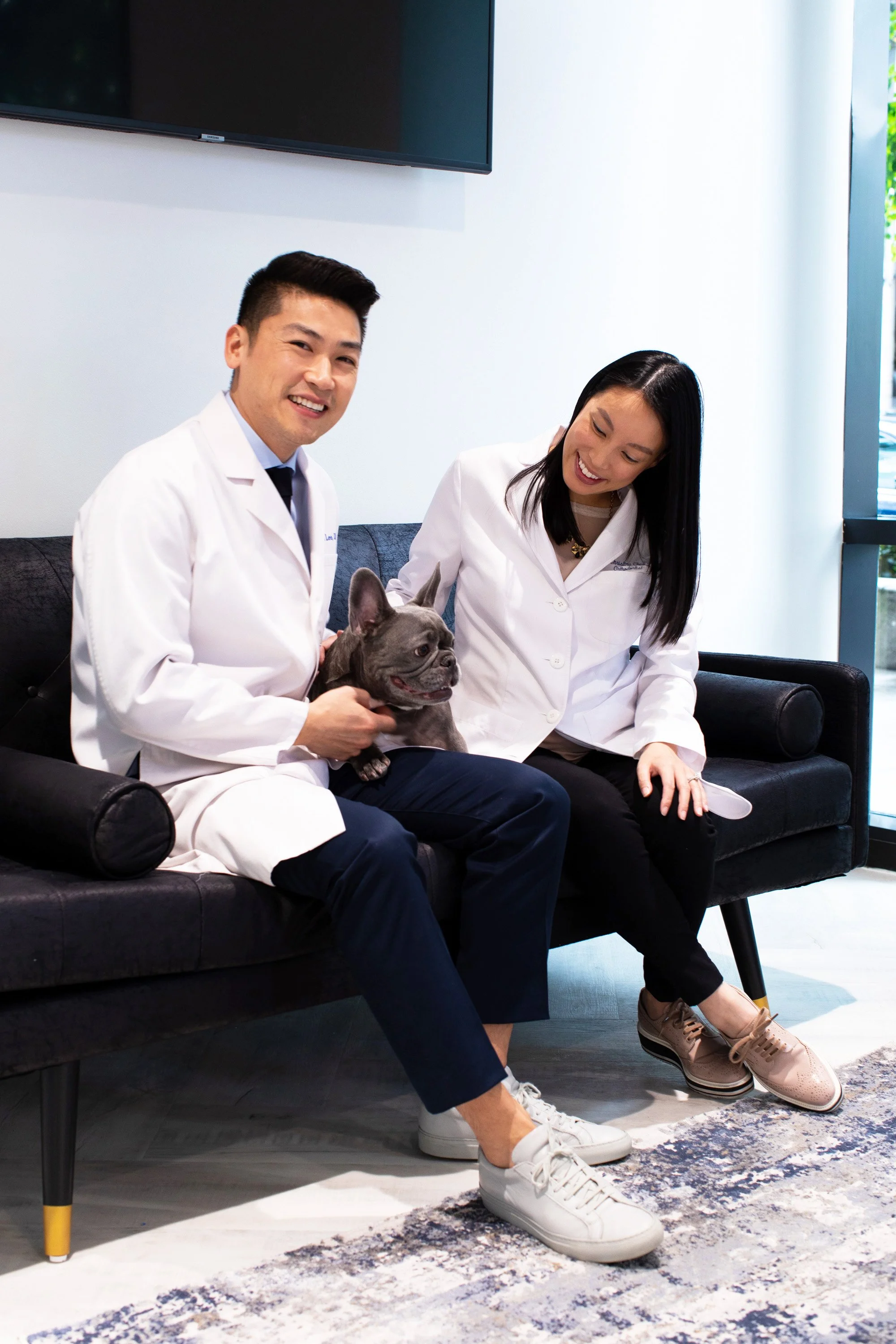 Dr. Daniel Lee and Dr. Christina Lee, founders of The Smile Space, relaxing with their French bulldog in the practice reception area.