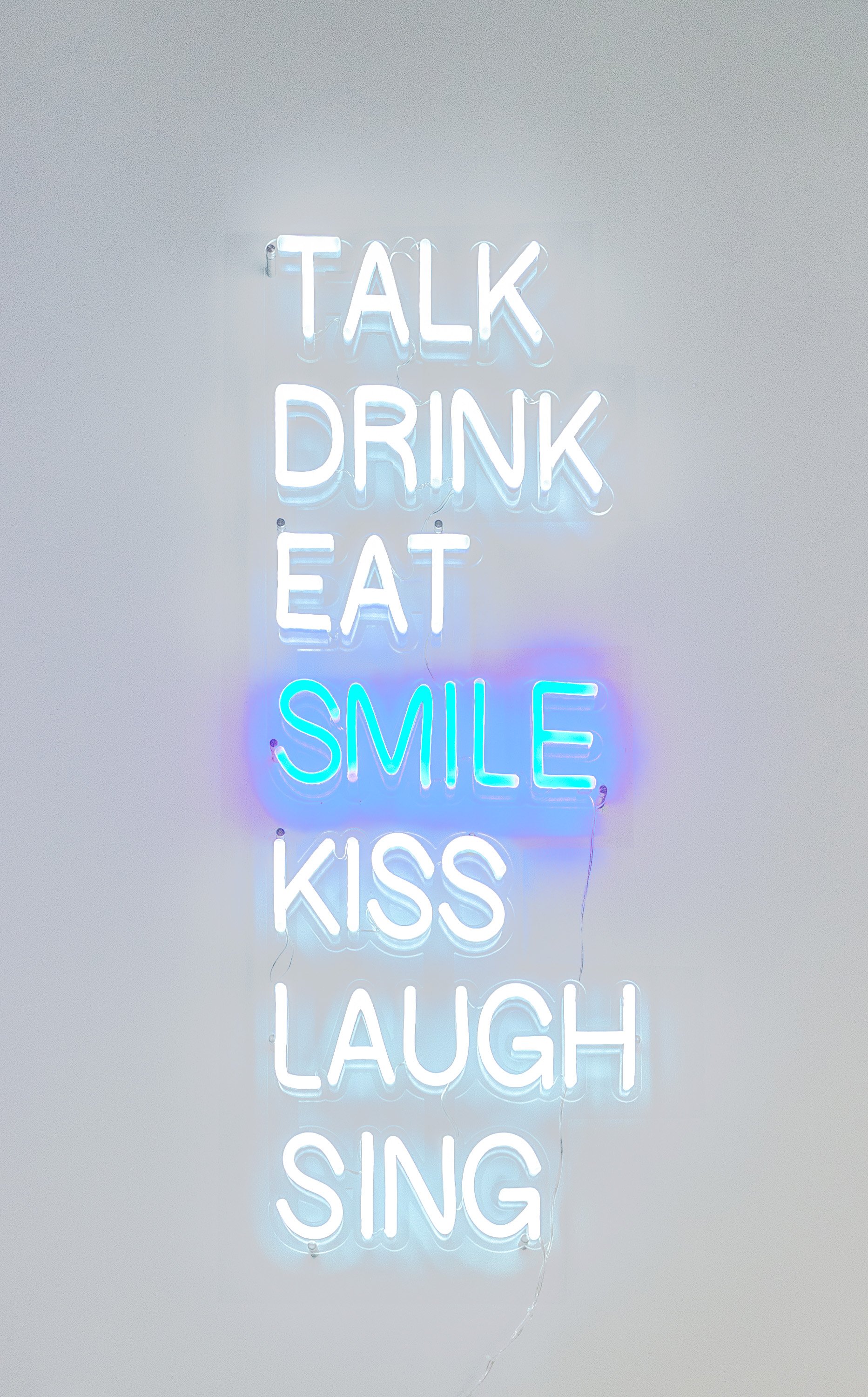 Neon wall sign at The Smile Space displaying the words "Talk Drink Eat Smile Kiss Laugh Sing."
