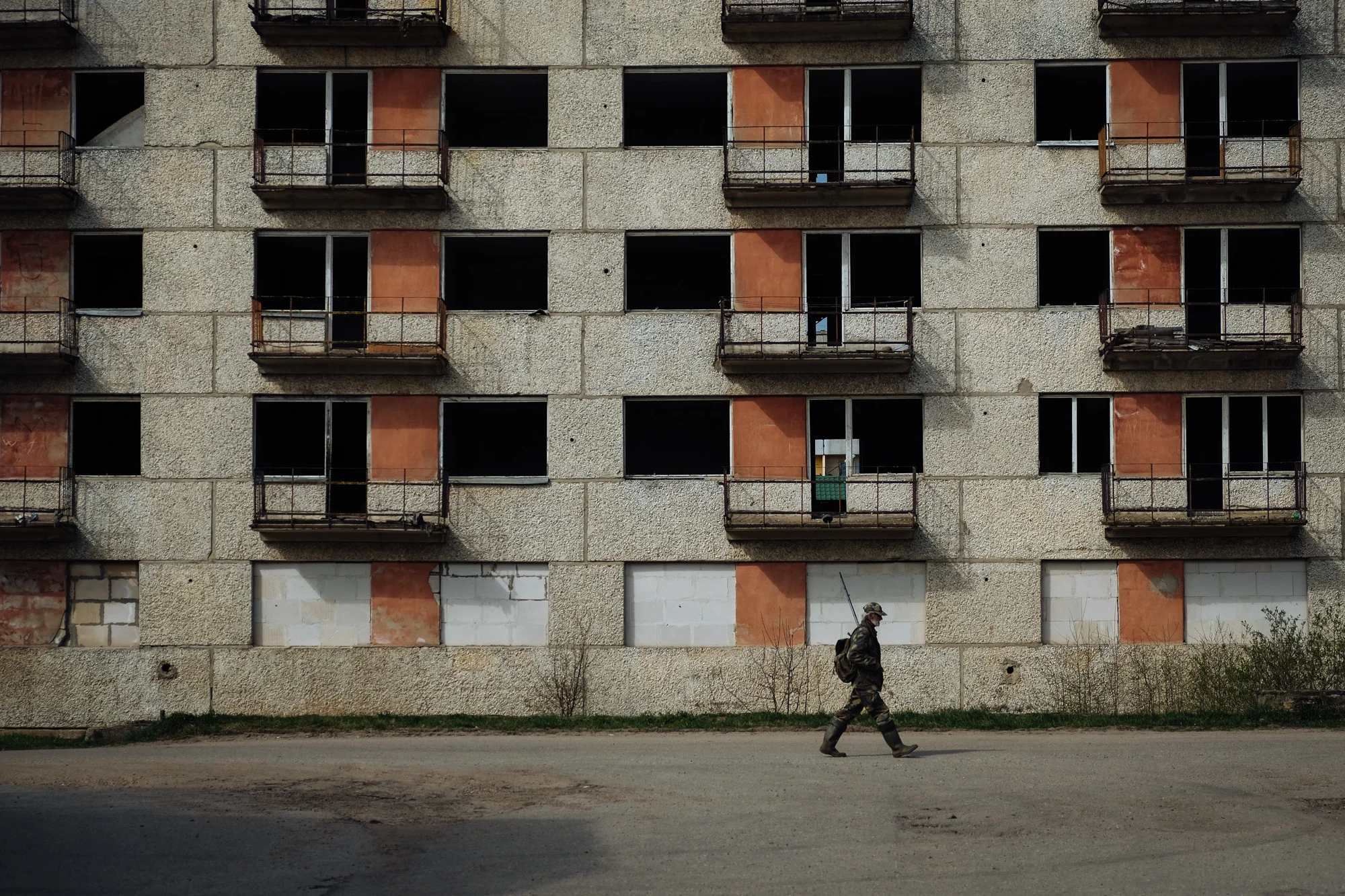 Jekabpils - Zemgale. A fisherman walks in front of an abandoned building in a neighbourhood of the city. The presence of unfinished and abandoned buildings is very high around the city.