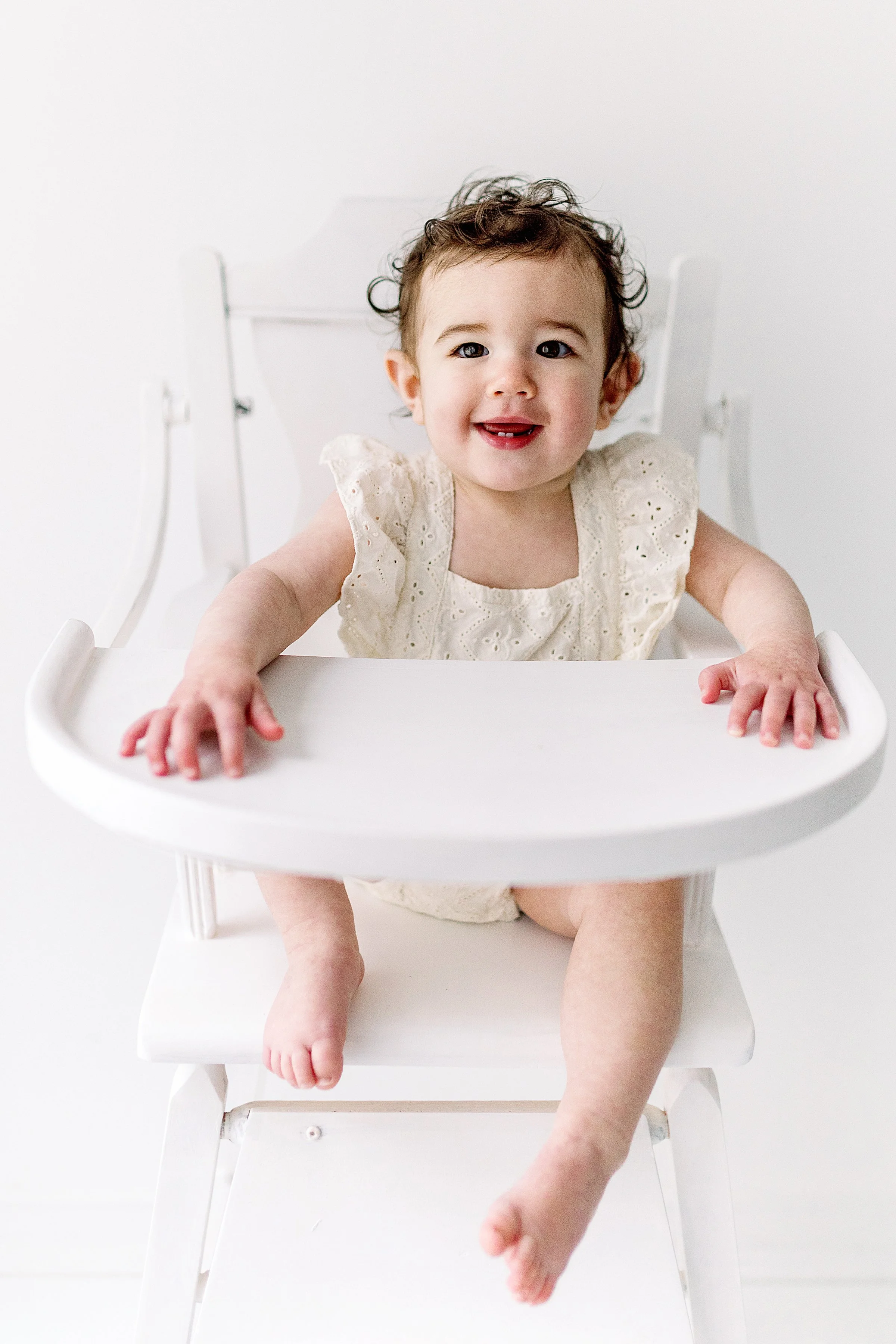 Sweet baby girl in a white high chair smiling at camera