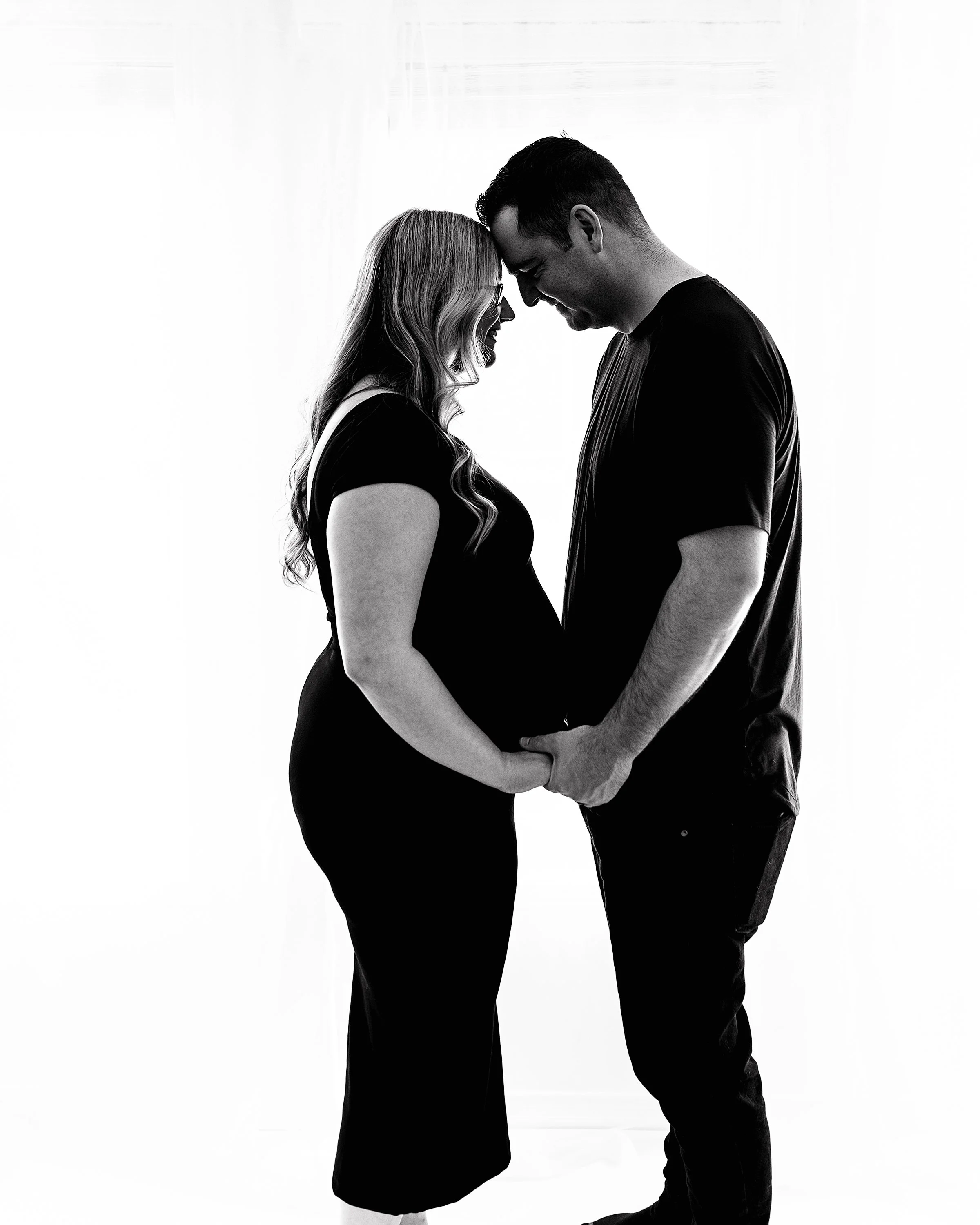 Black and white maternity couple holding hands and heads touching looking at belly