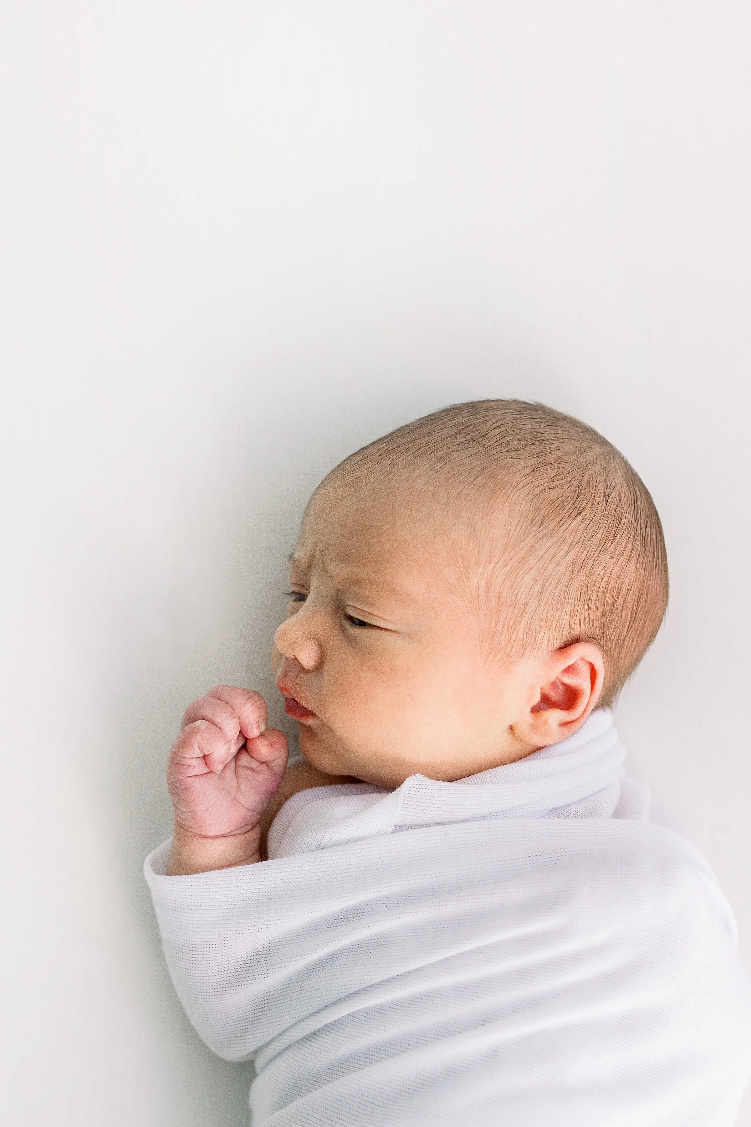 Close up of sleepy baby boy in white linen