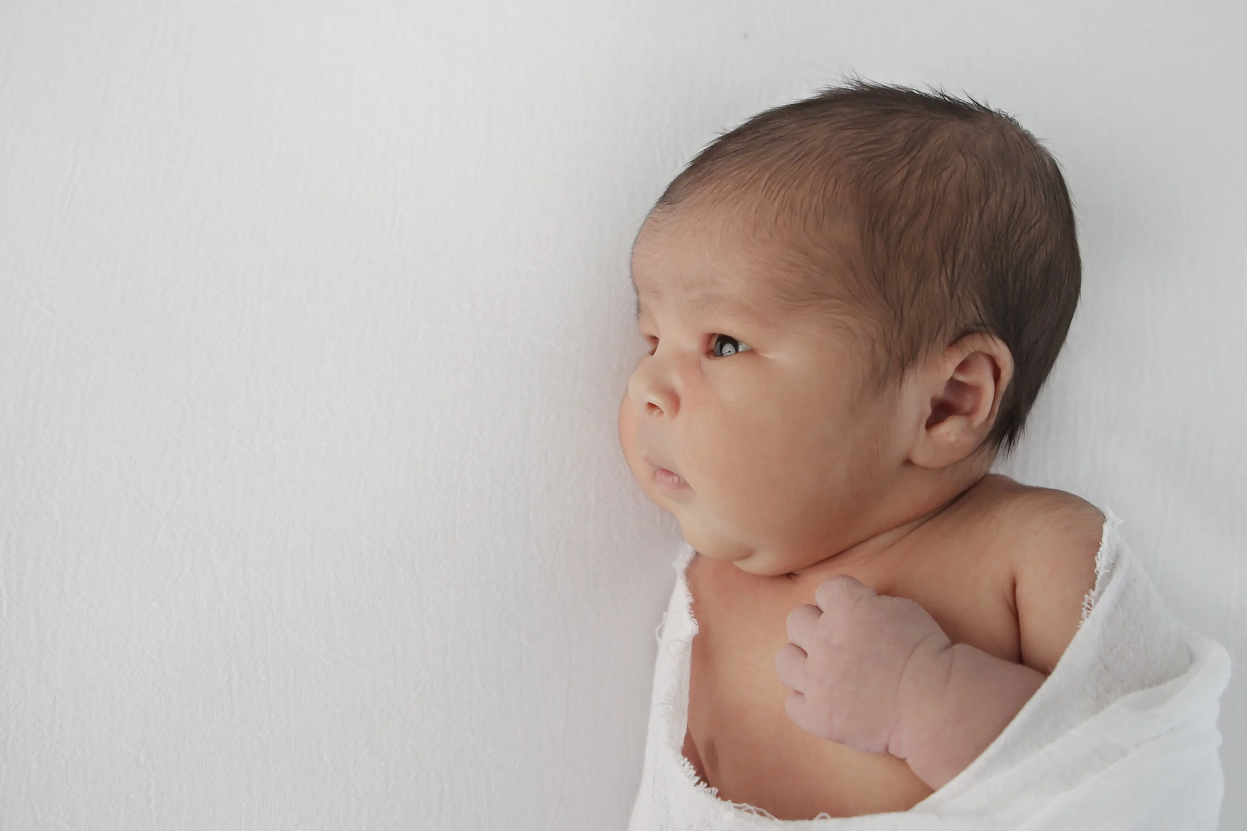 Wide away newborn wrapped in white on white background in Durham Region