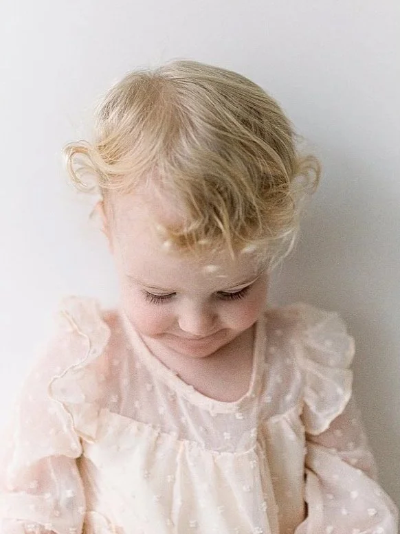 Classic portrait of a one year old baby girl wearing a frilly pink dress looking down and focus is on her eyelashes during a baby session in Durham Region