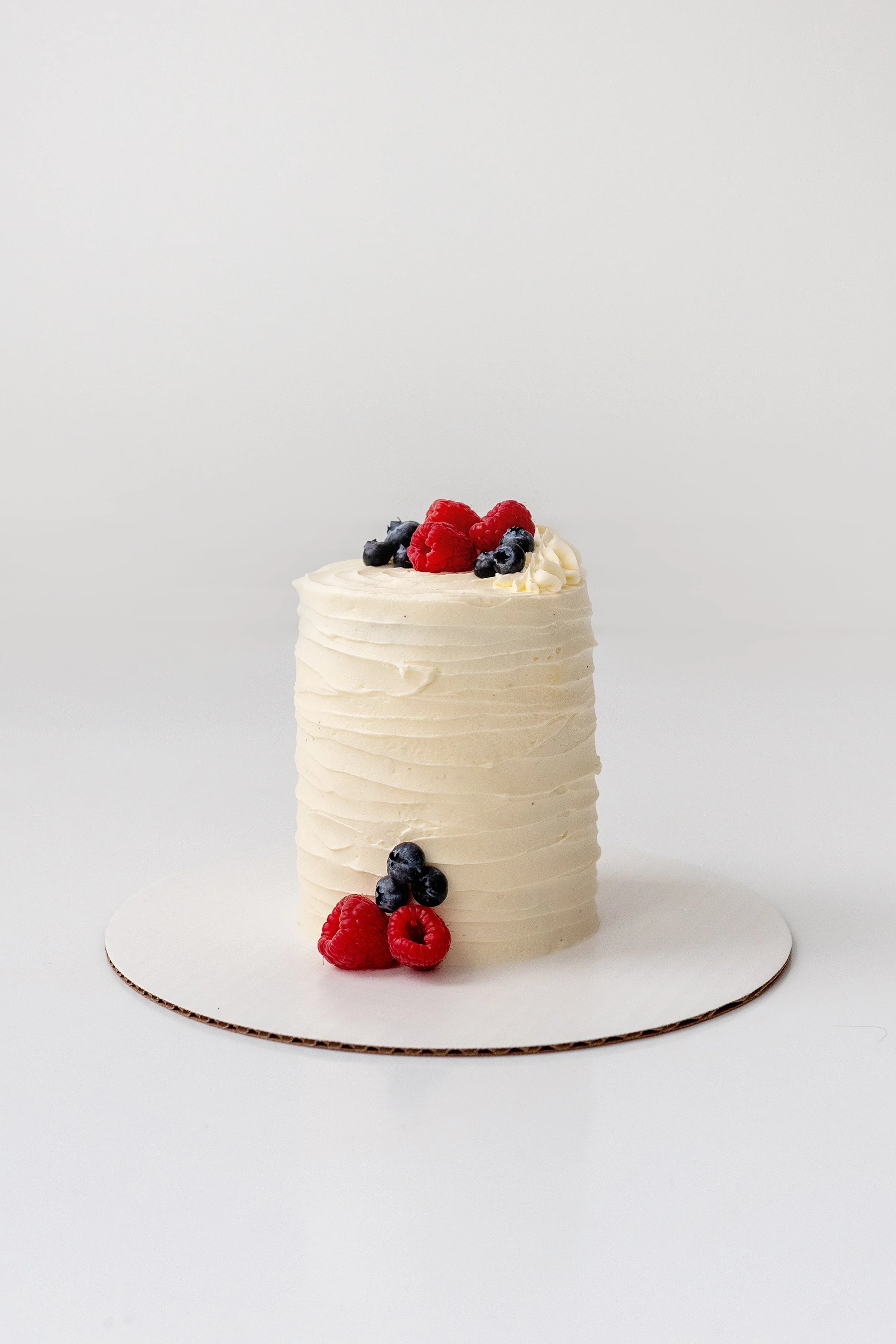 Classic buttercream cake with fresh berries on the floor in a white studio, Oshawa