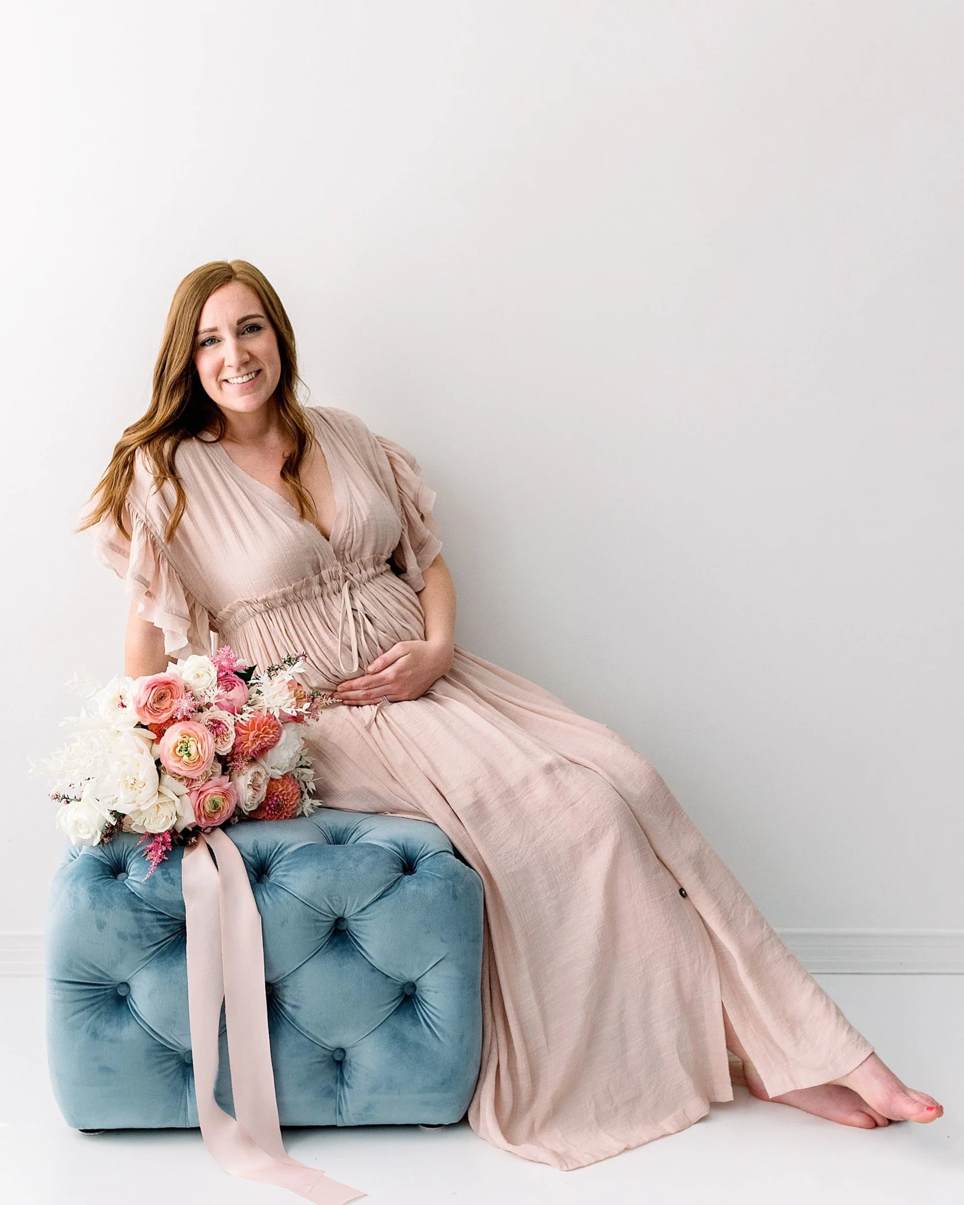 Pregnant mom to the sitting on blue ottoman with beautiful bouquet of flowers next to her
