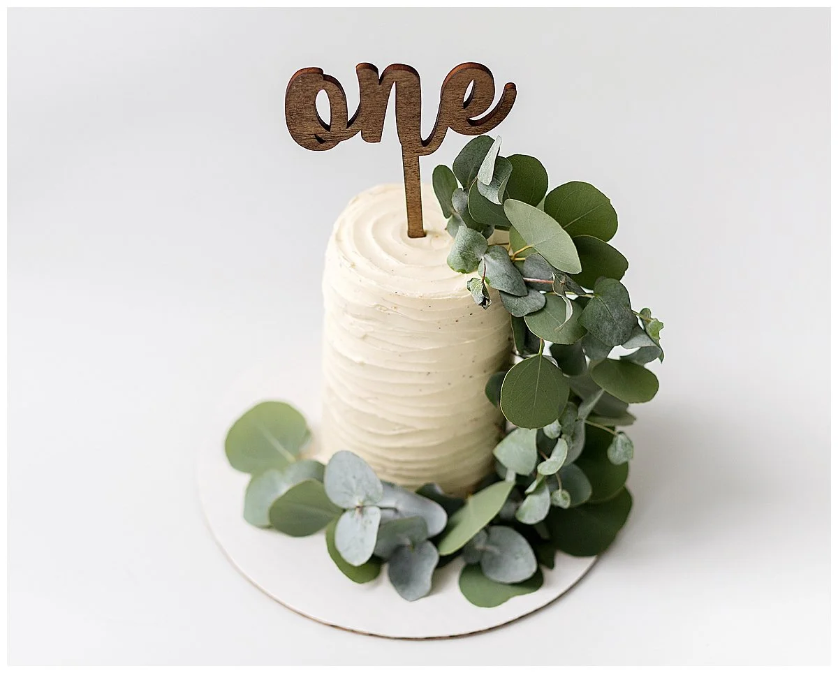 White buttercream cake with green eucalyptus  and a wooden number one cake sign, in Oshawa baby studio