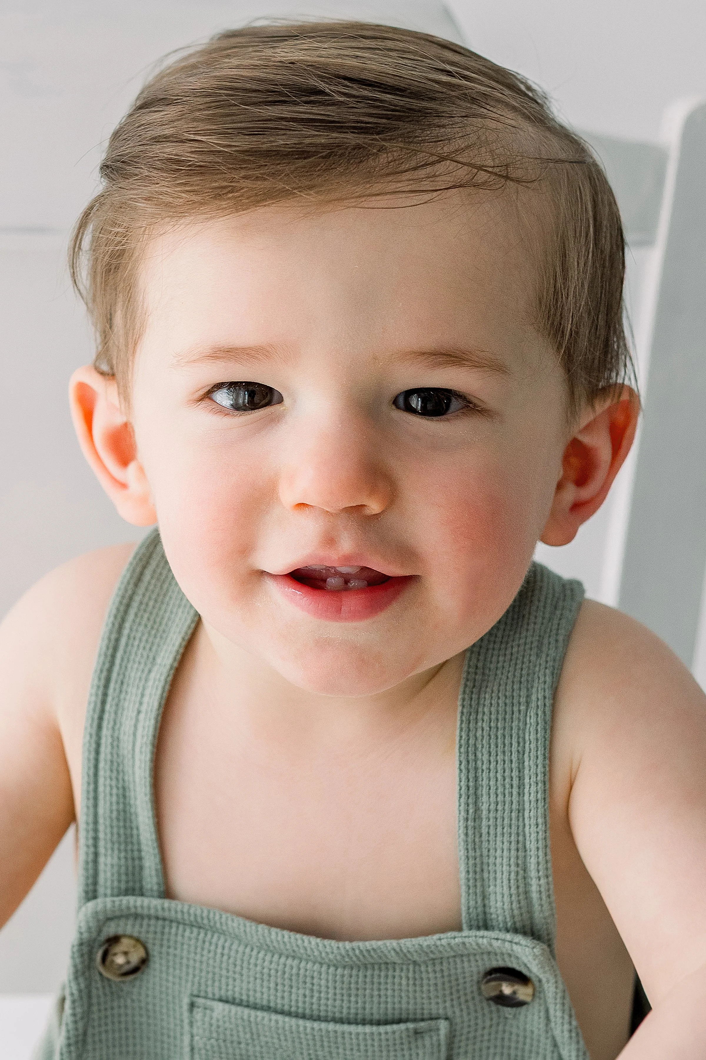 One year old baby boy portrait wearing a light green romper looking at camera smiling during his baby shoot in Oshawa