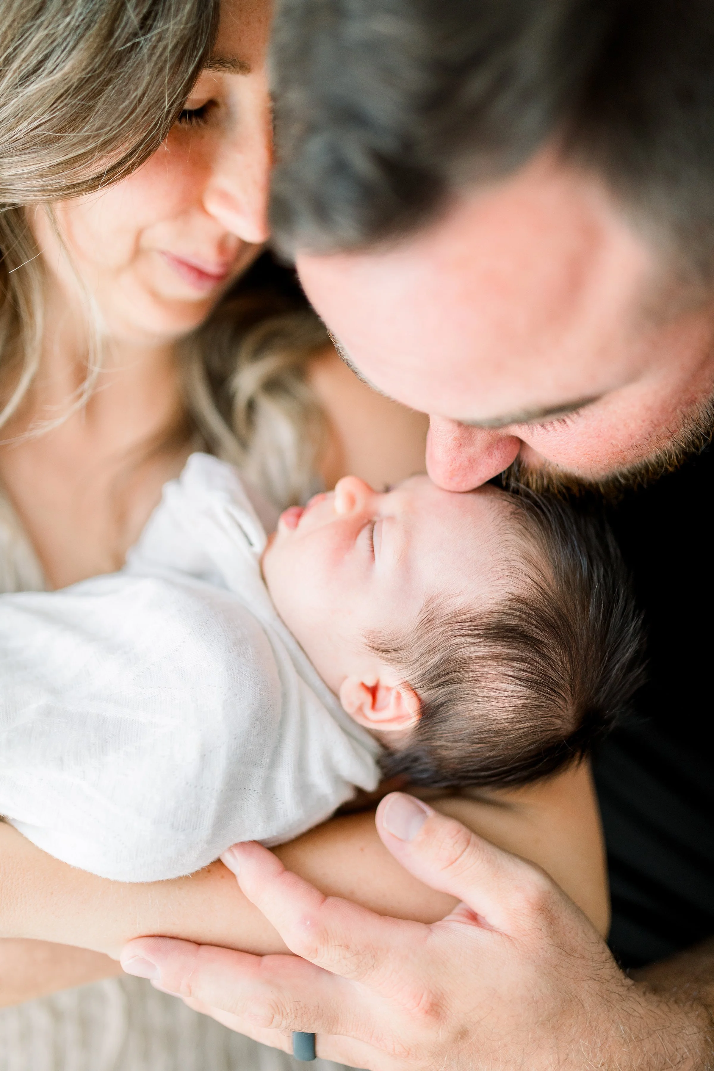 Sleeping newborn in moms arms while dad kisses baby head