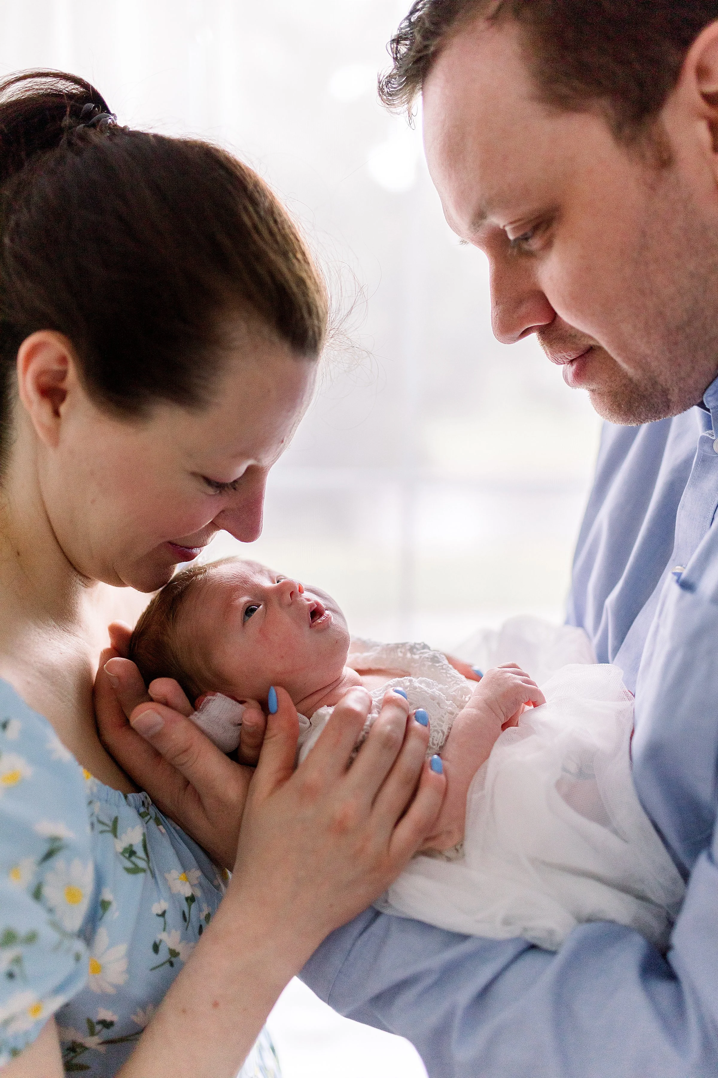 Newborn photo of mom and dad holding baby in front of window in Oshawa studio