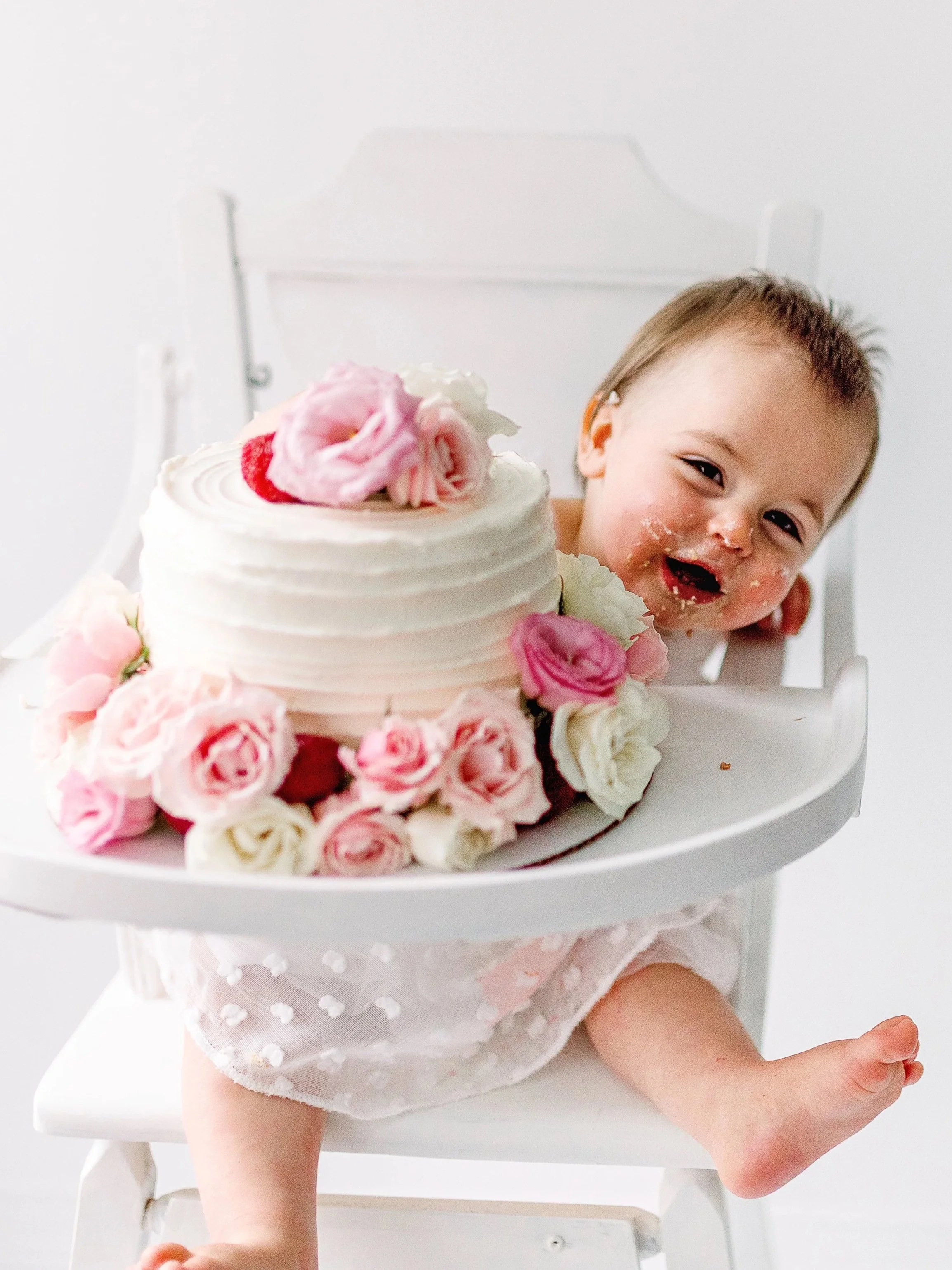 Baby girl icing on face playing peek a boo behind floral cake
