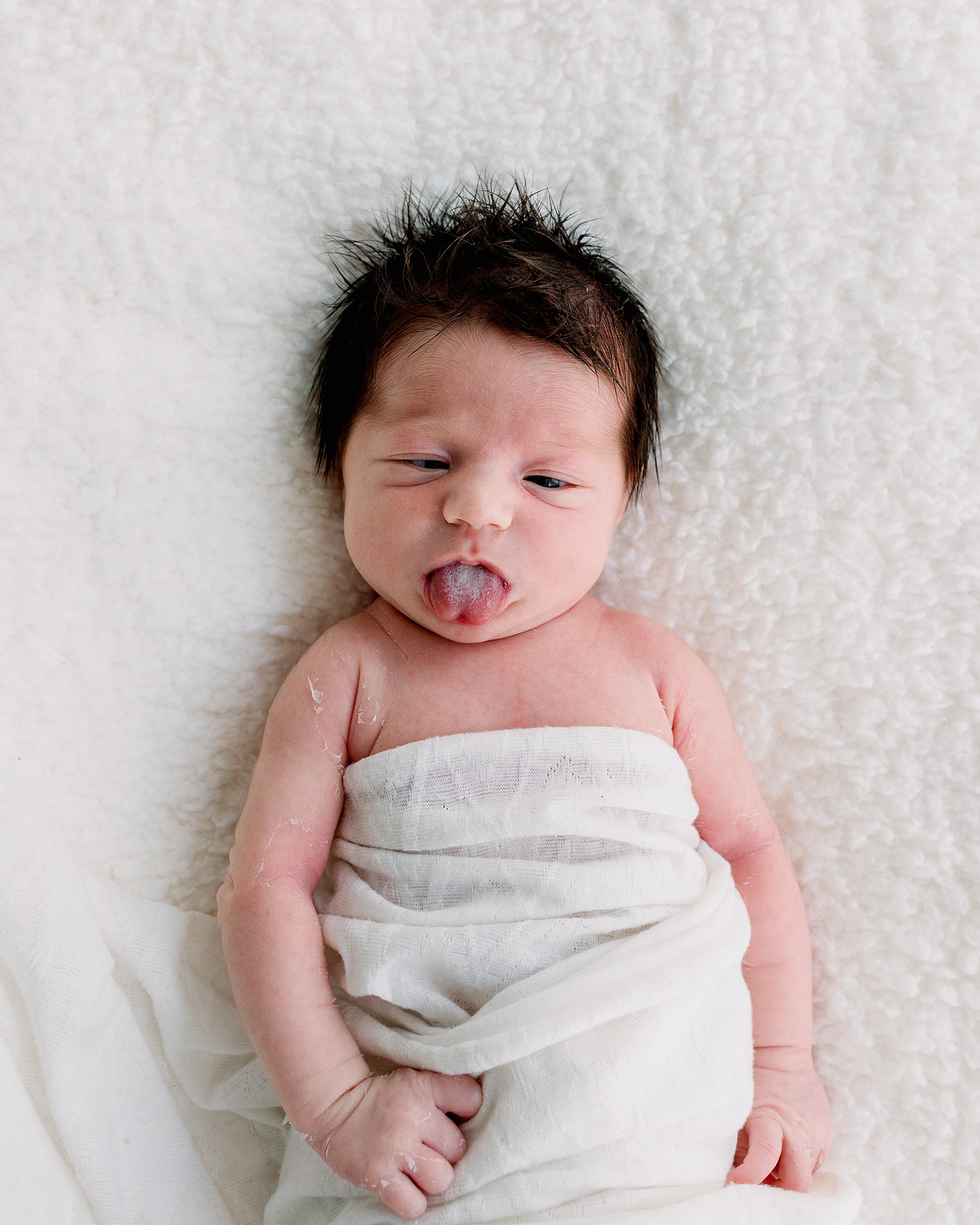 Newborn sticking out tounge on white blanket in Oshawa Durham Region studio