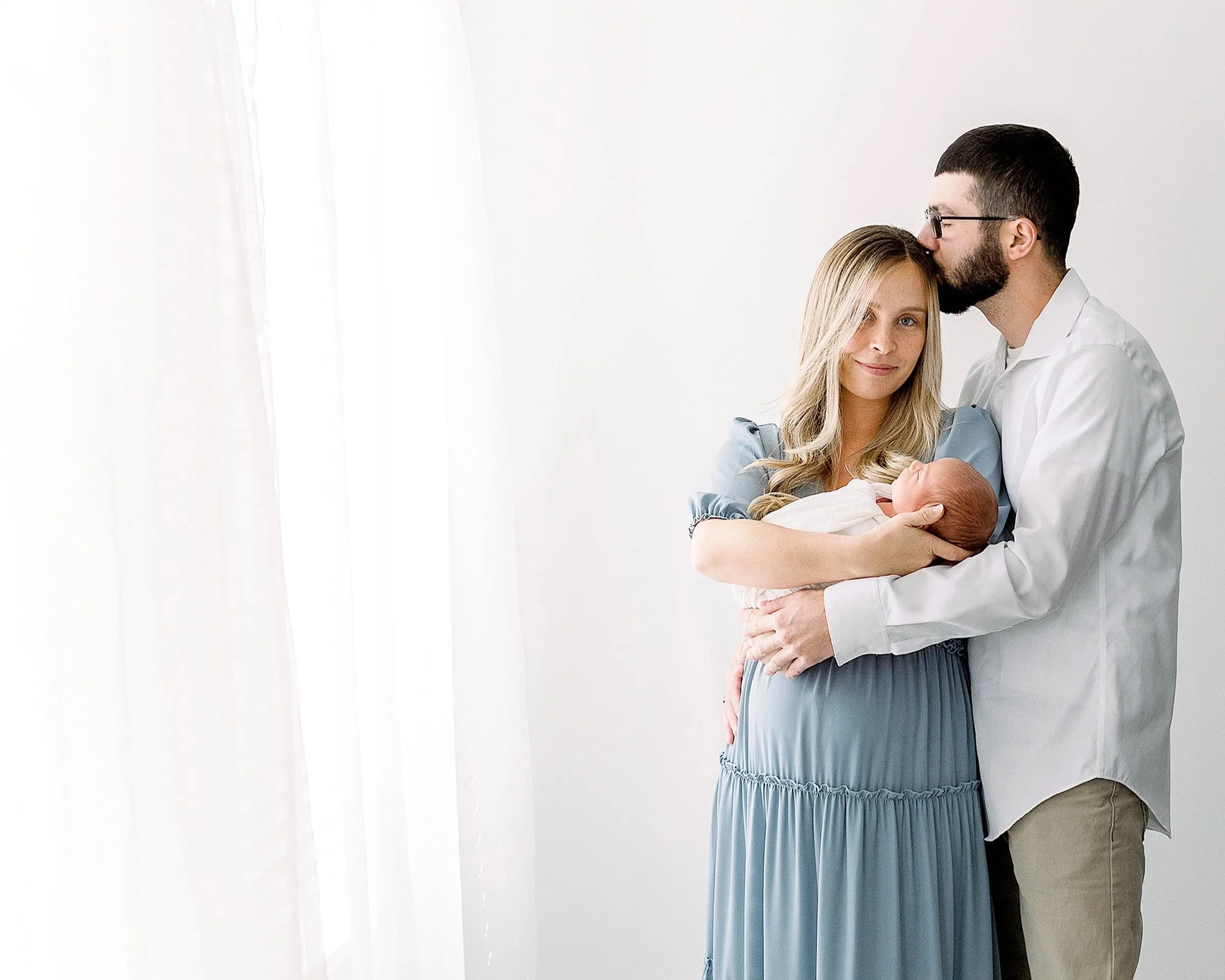 Beautiful image of mom and dad holding newborn baby in a white studio