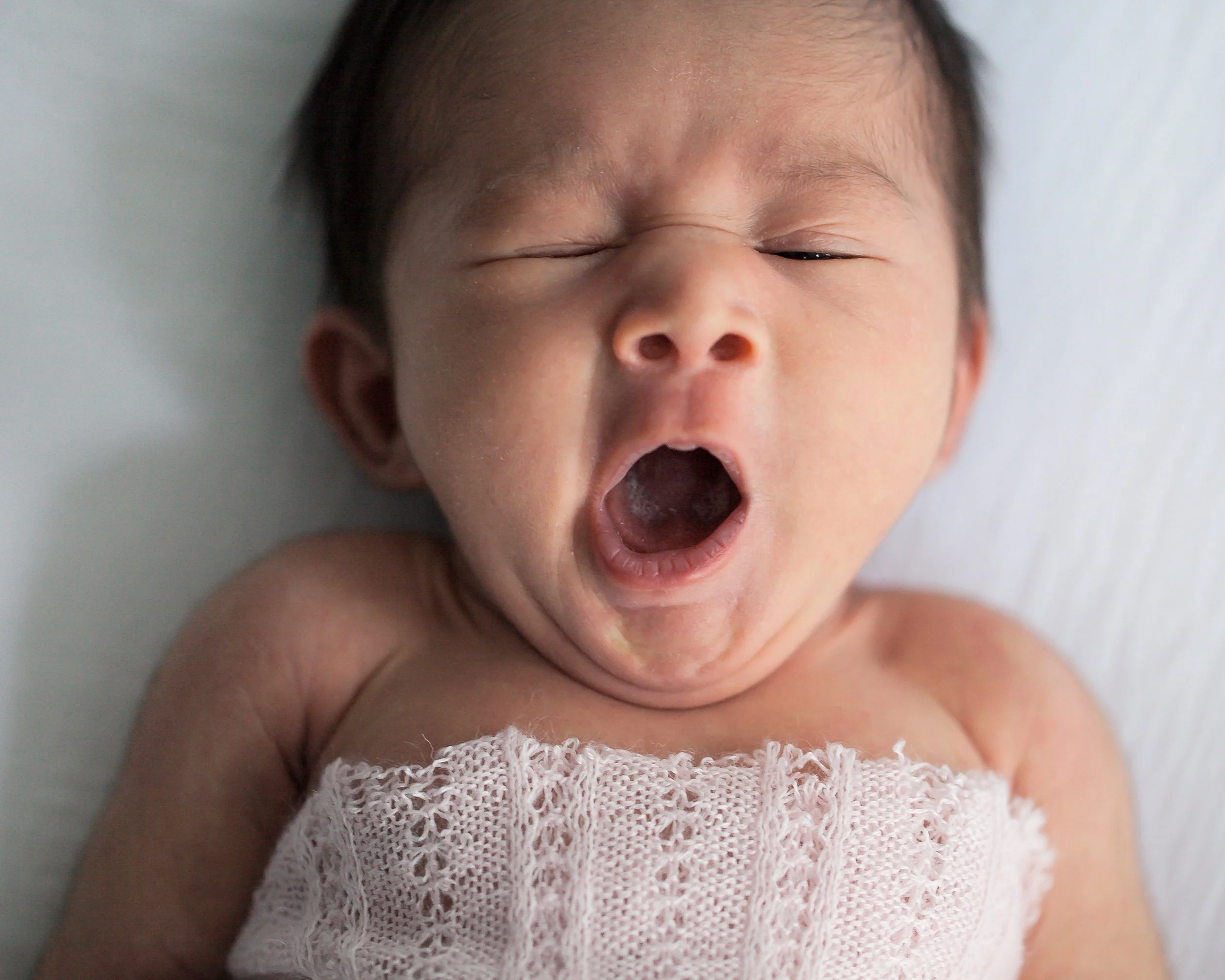 Yawning newborn in pink studio wrap in Oshawa