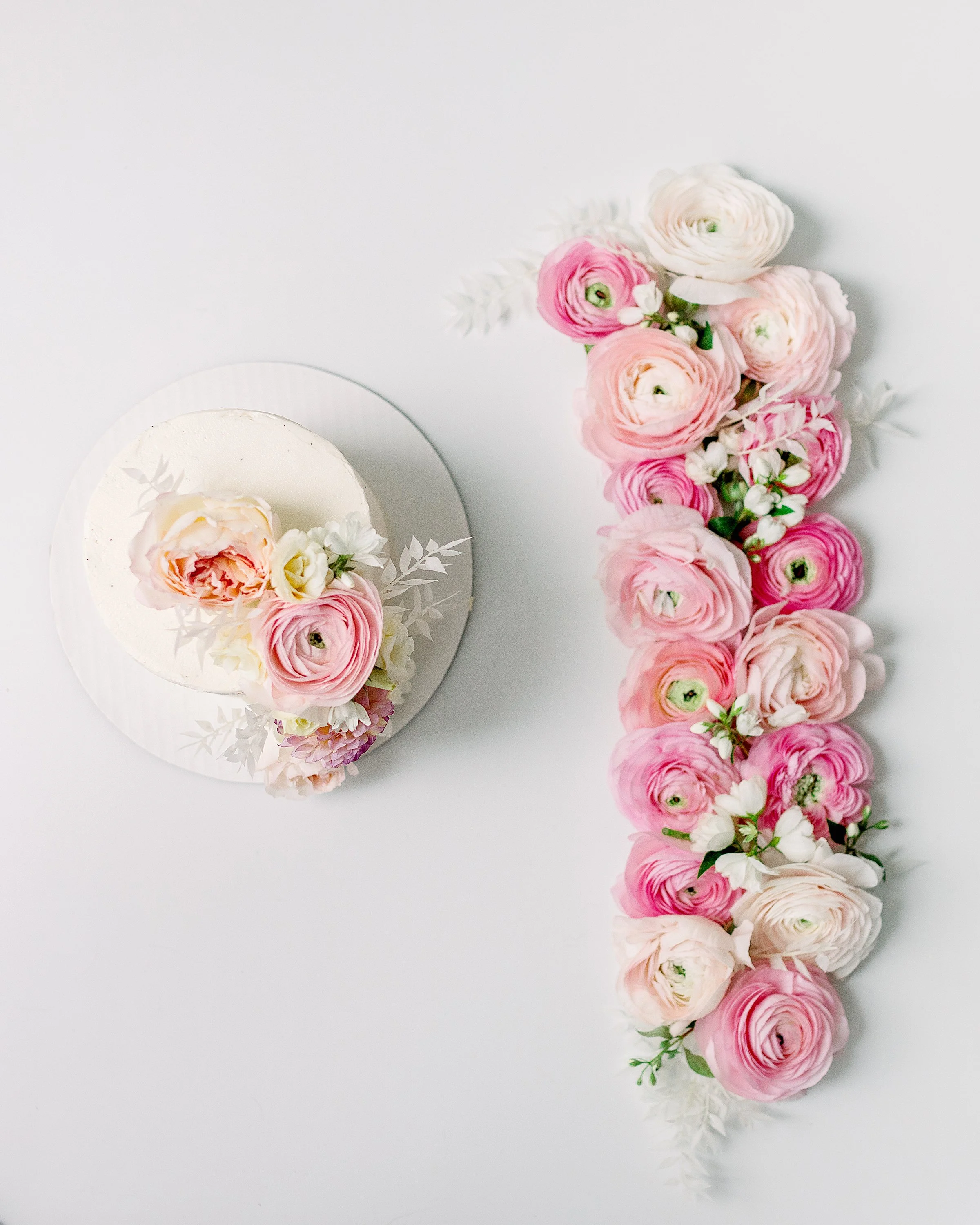 White cake with pink roses on it and a floral number made of roses and ranunculus on white floor in Oshawa motherhood studio