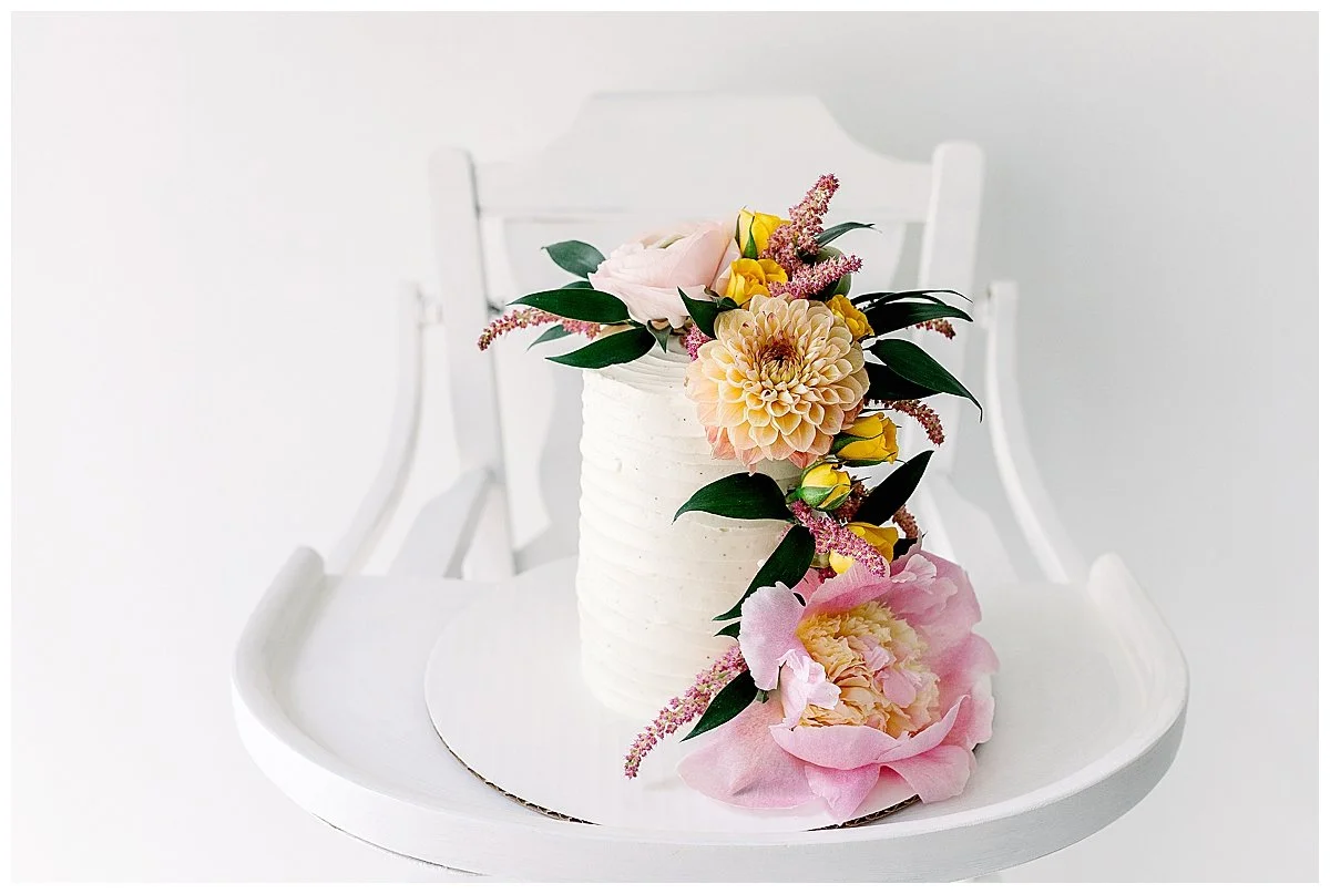 Gorgeous white buttercream cake with a pink peony and yellow dahlia on a white highchair, in Durham Region studio