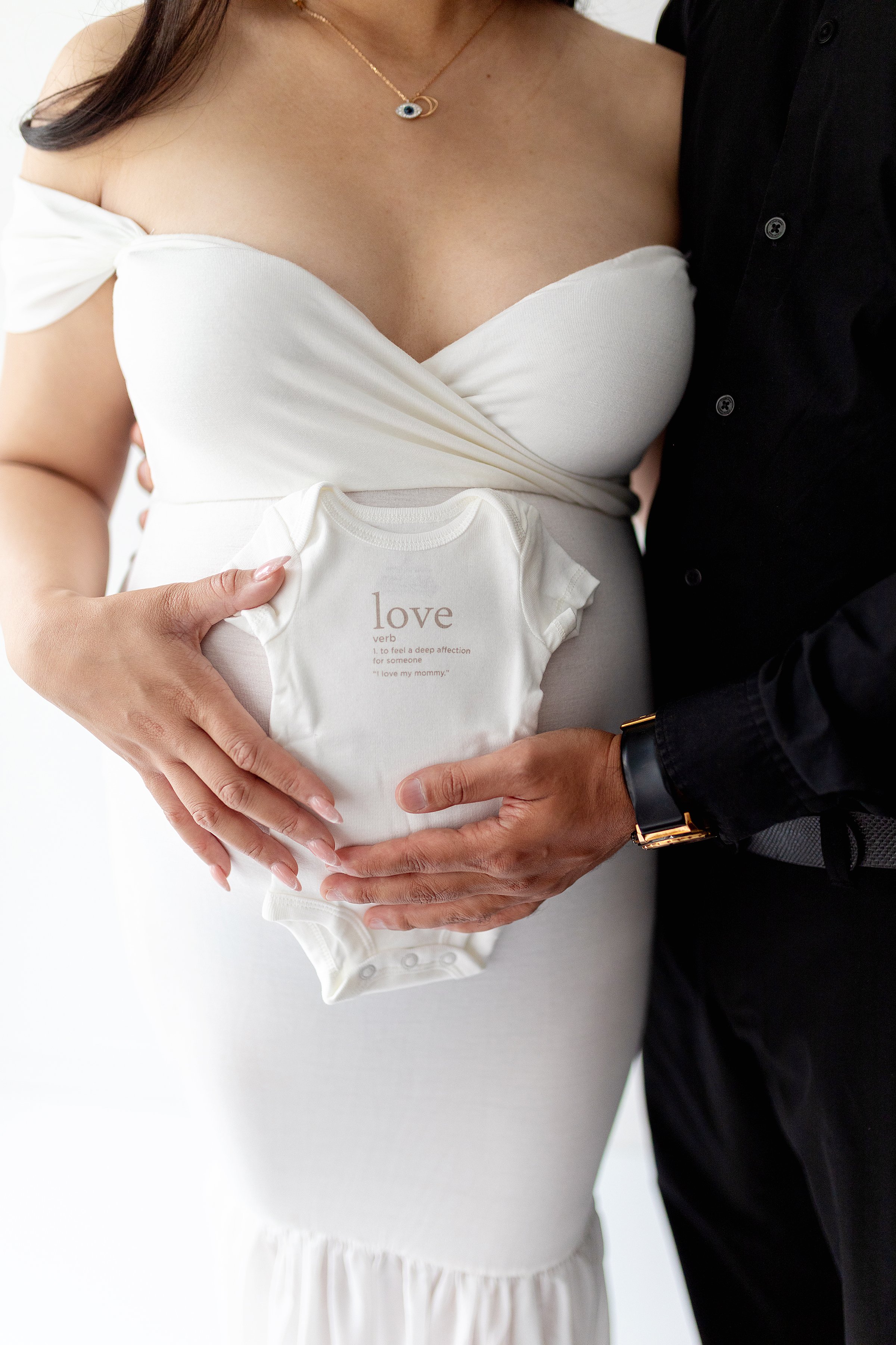 Maternity couple holding white onesie on belly 