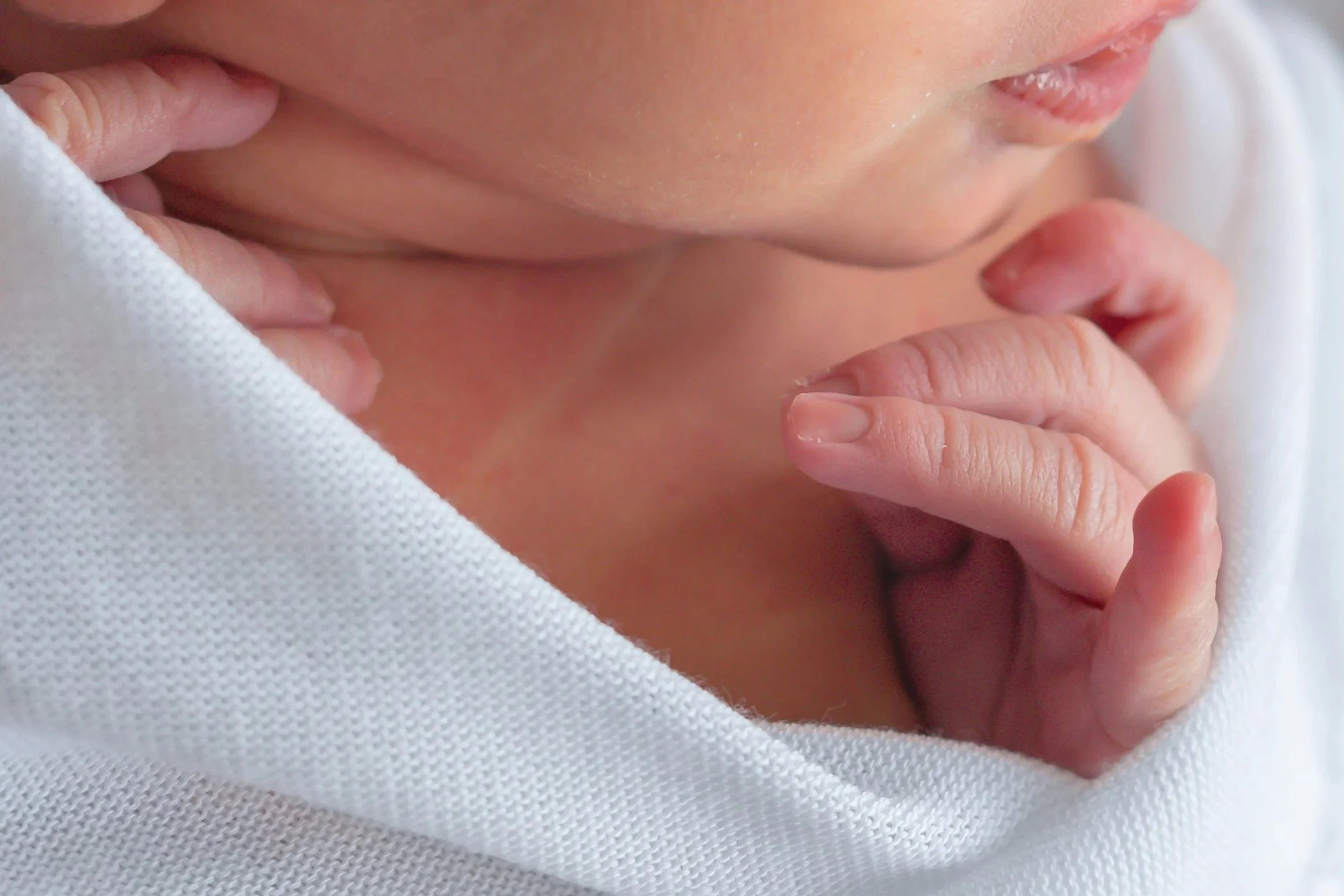 Close-up of a newborn baby's lips  with hand near mouth, wrapped in white fabric.