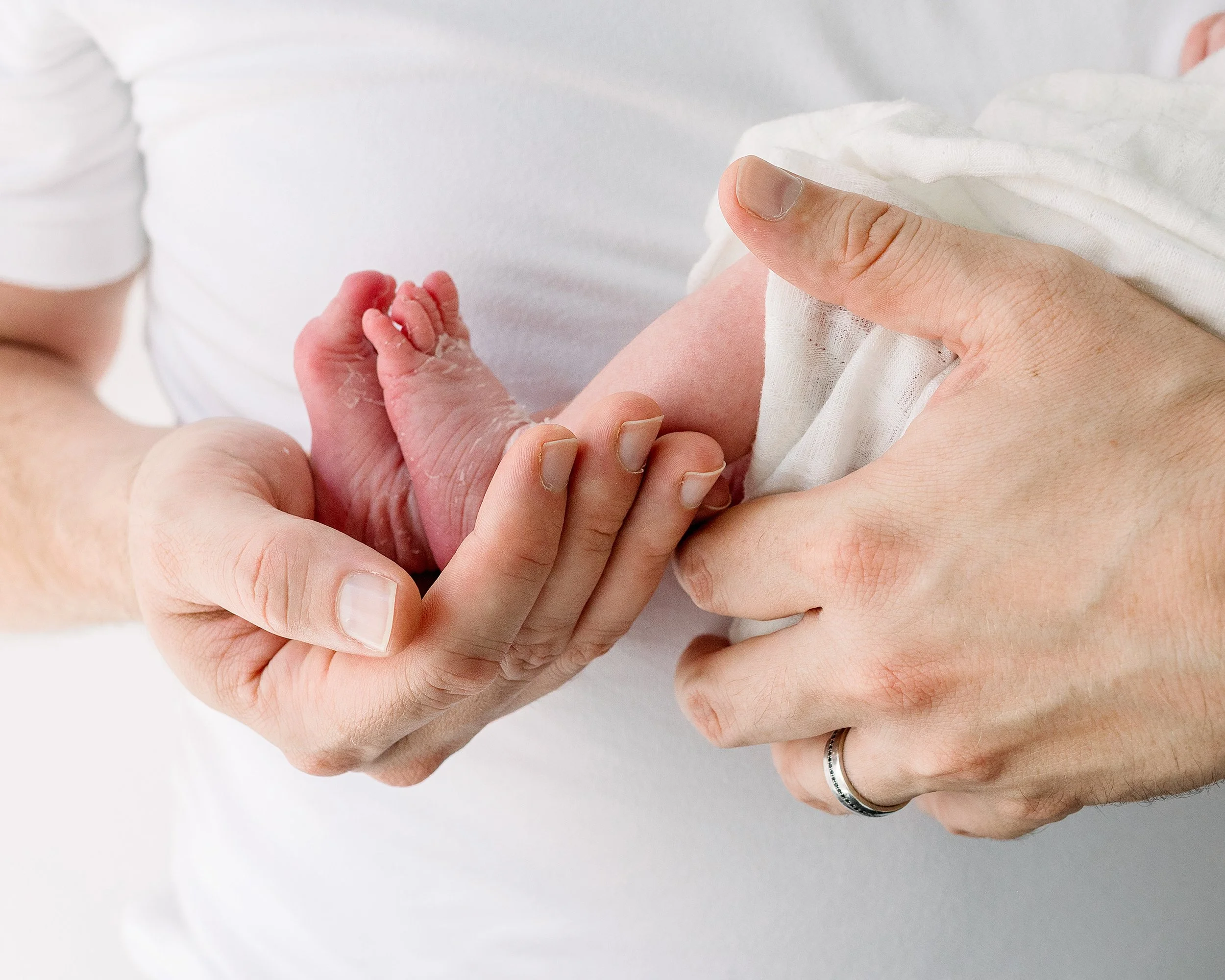 New Dad wearing white holding his newborns baby feet in Oshawa studio