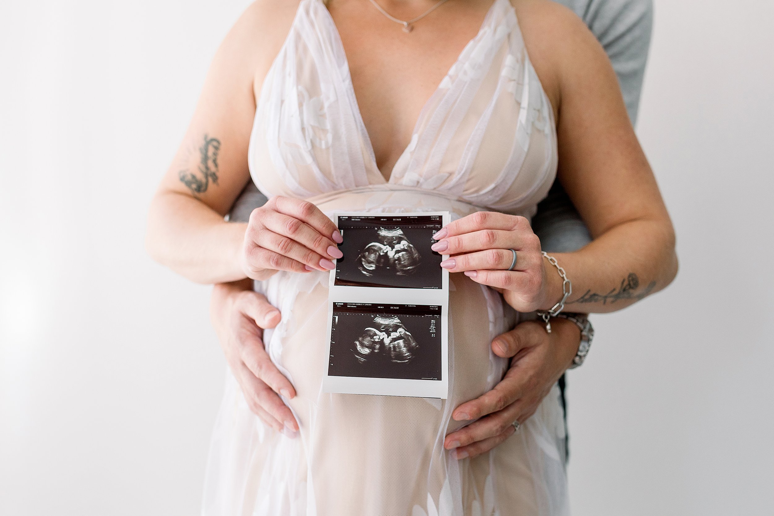 Close up of baby ultrasound with mom in nude gown and dad holding mom to be pregnant belly