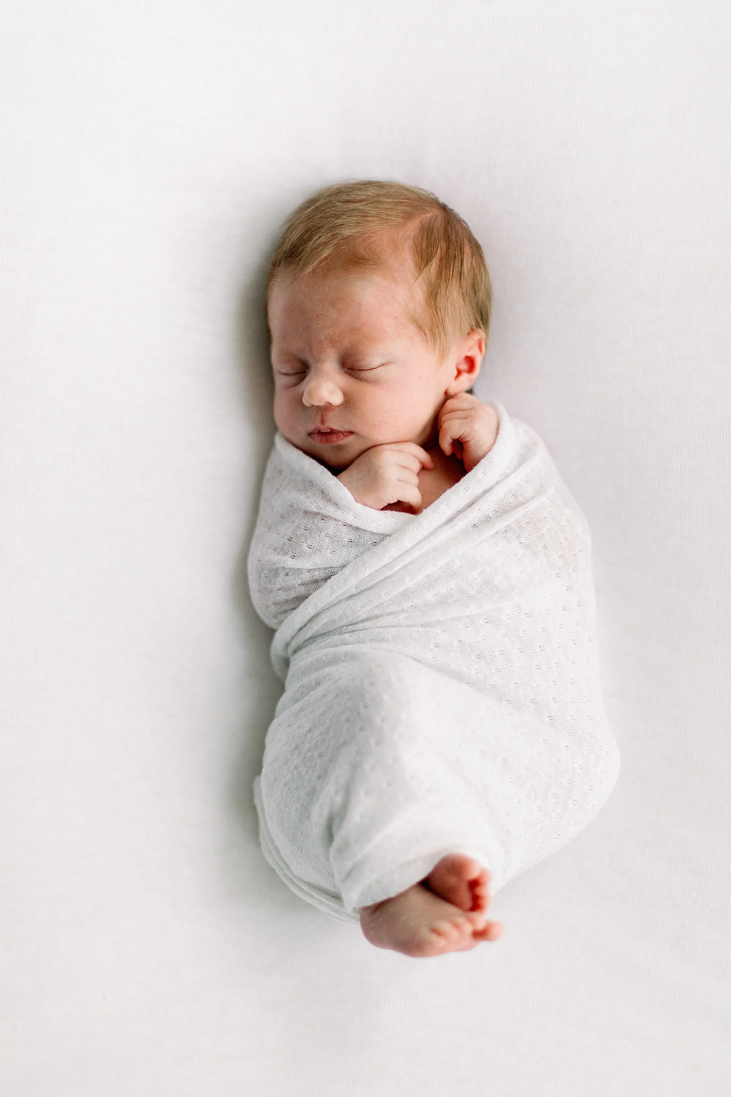 Red headed newborn swaddled in white sleeping in Oshawa Baby Studio