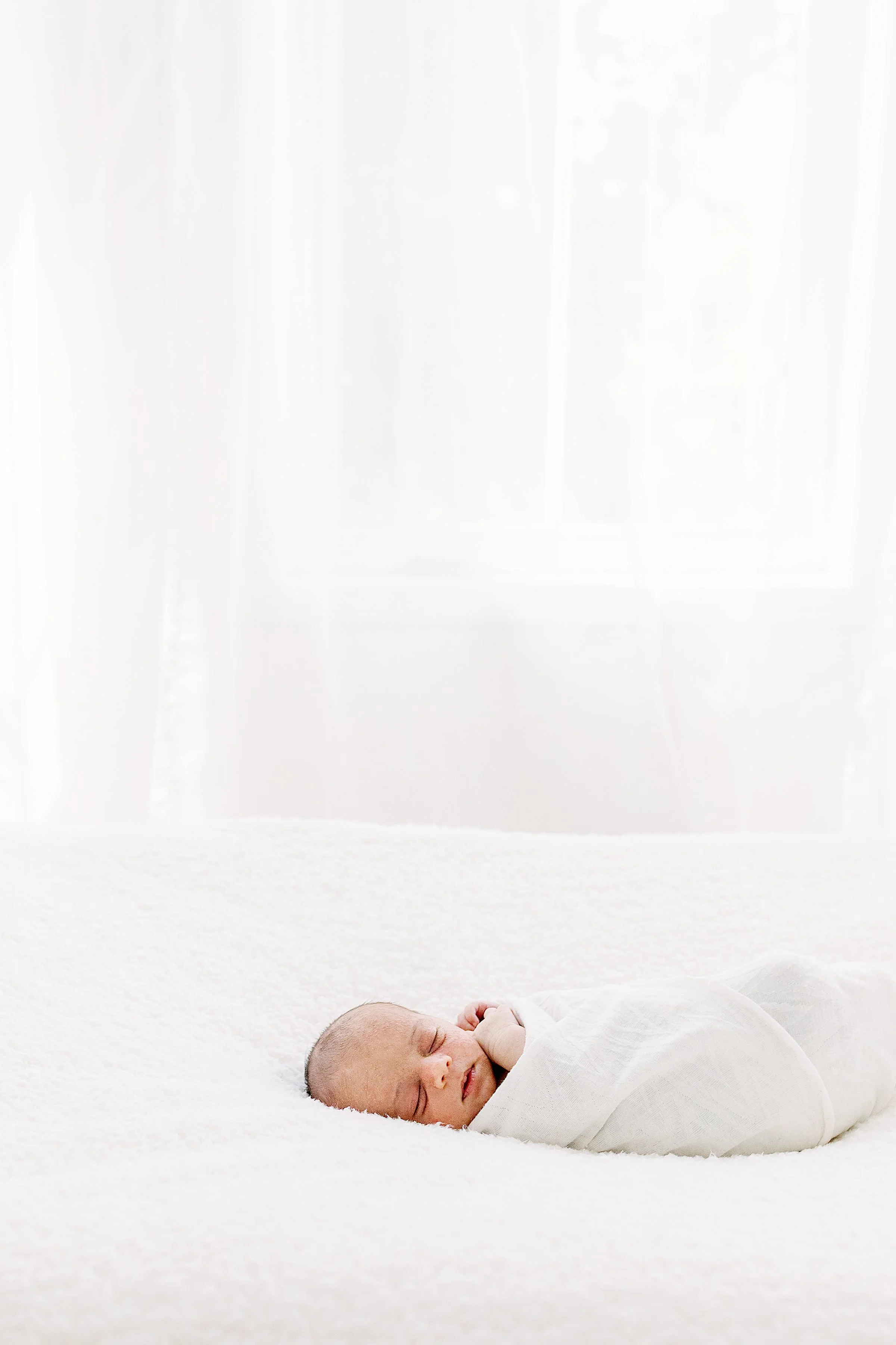 Sleeping baby wrapped in white on white blanket