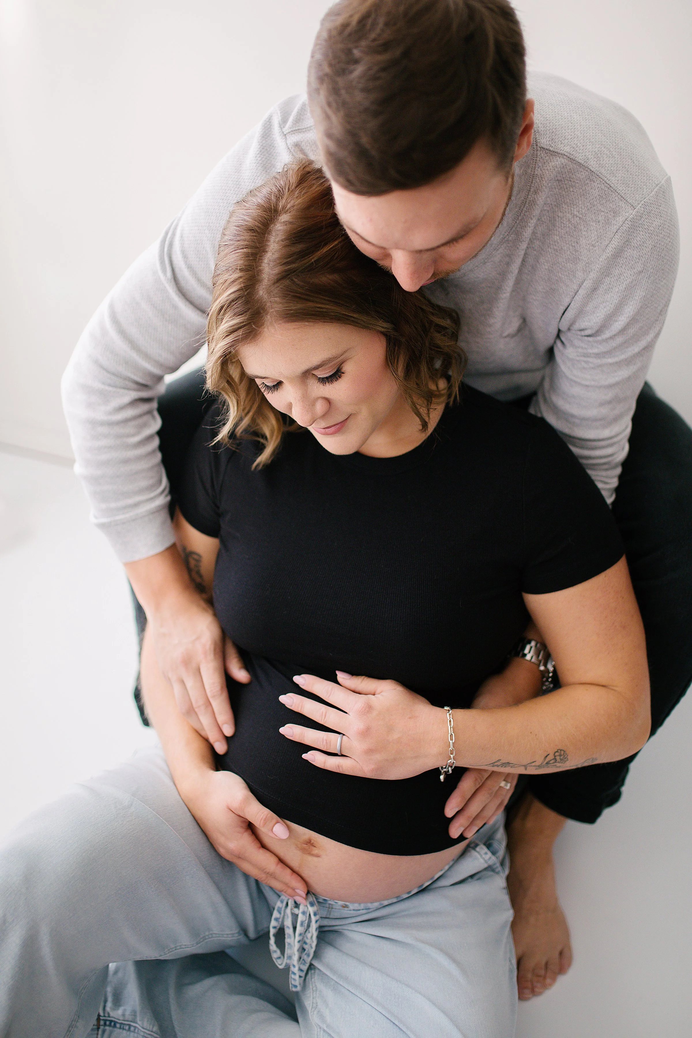 Cute maternity couple sitting down holding belly