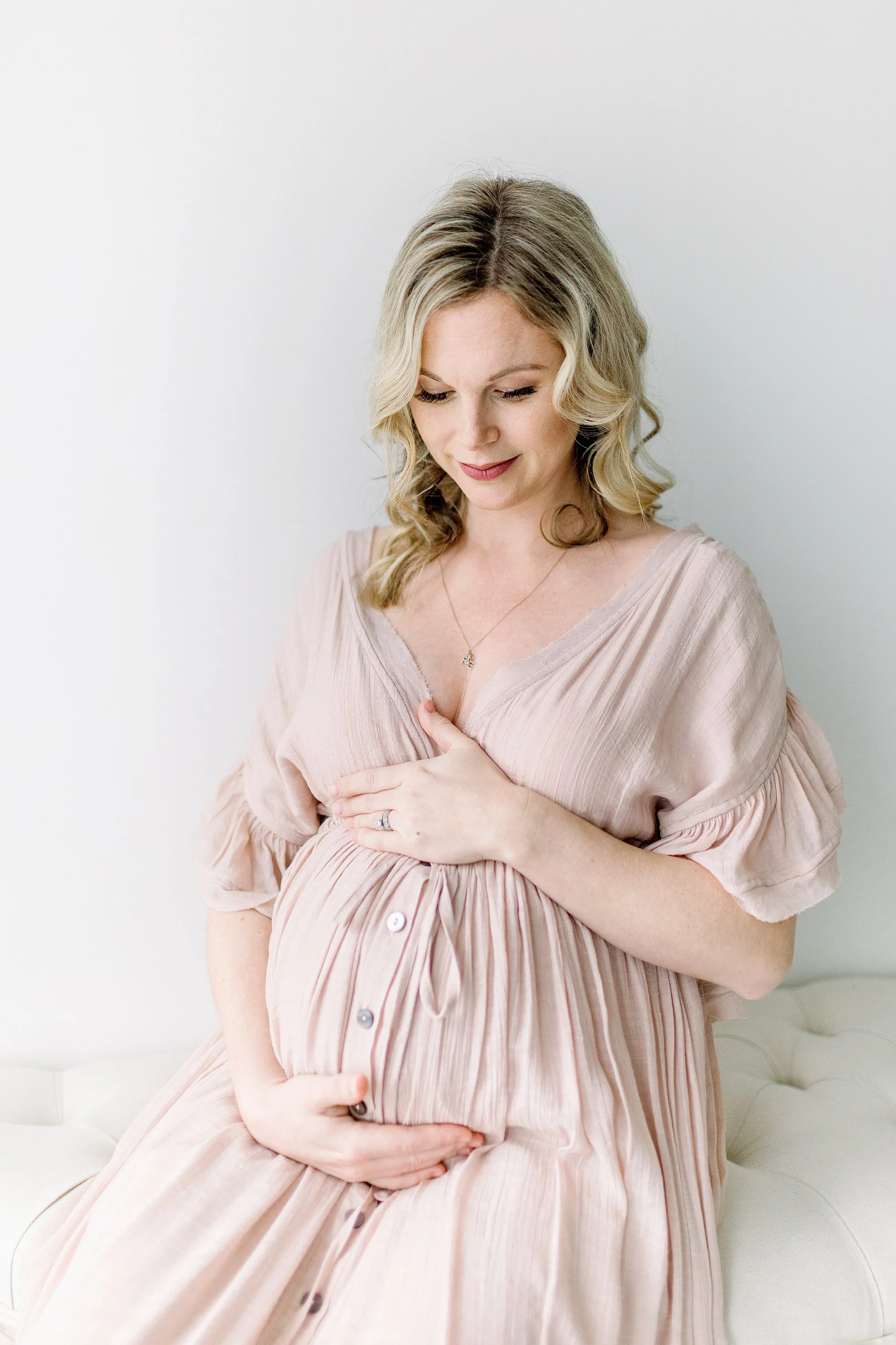 Beautiful pink pastel dress on mom to be holding belly while sitting down