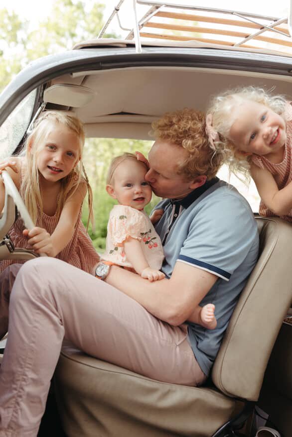 Sad sits in driver sit of Volkswagon with three daughters around him