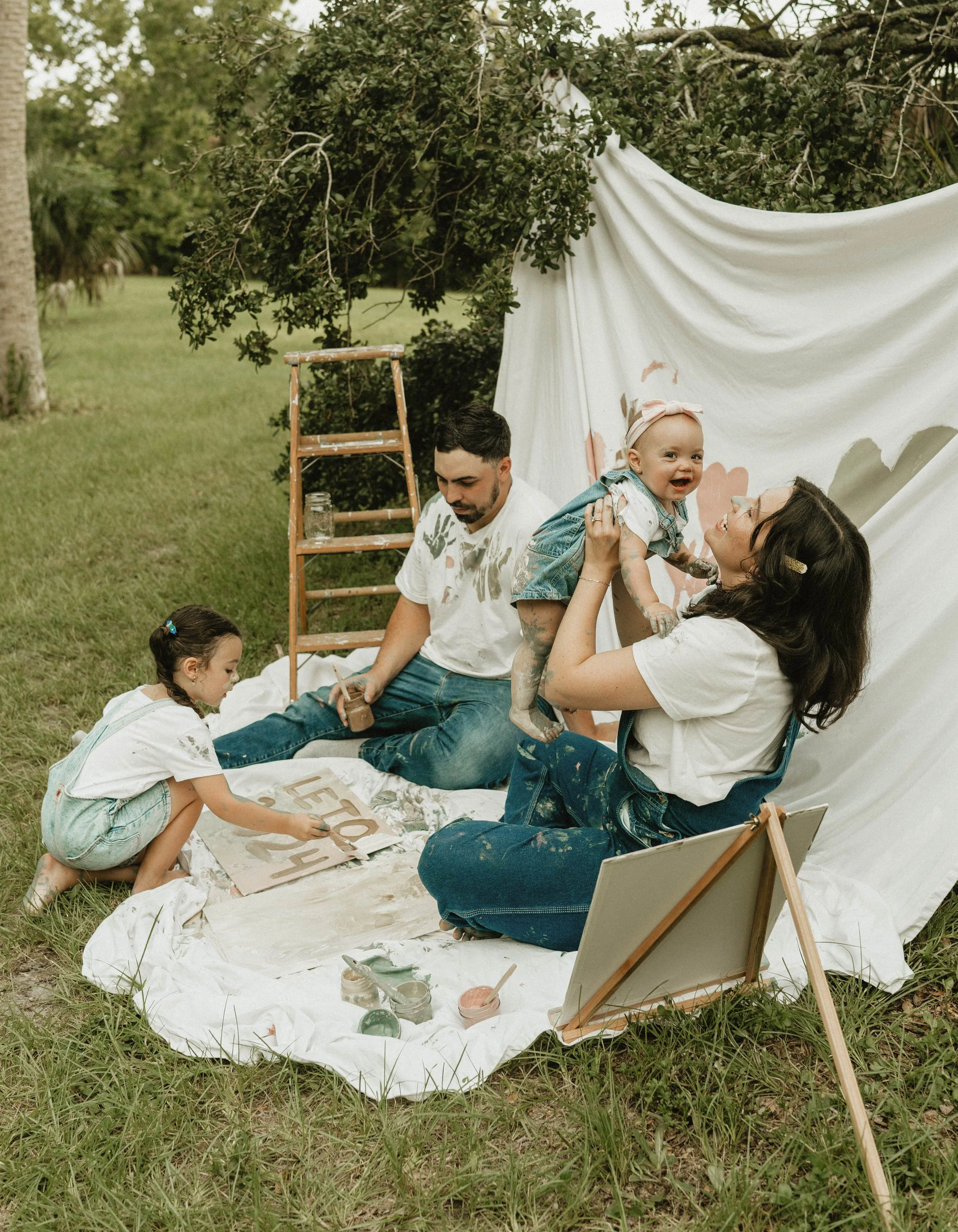 Family sitting on drop cloth in jeans and white shirts painting