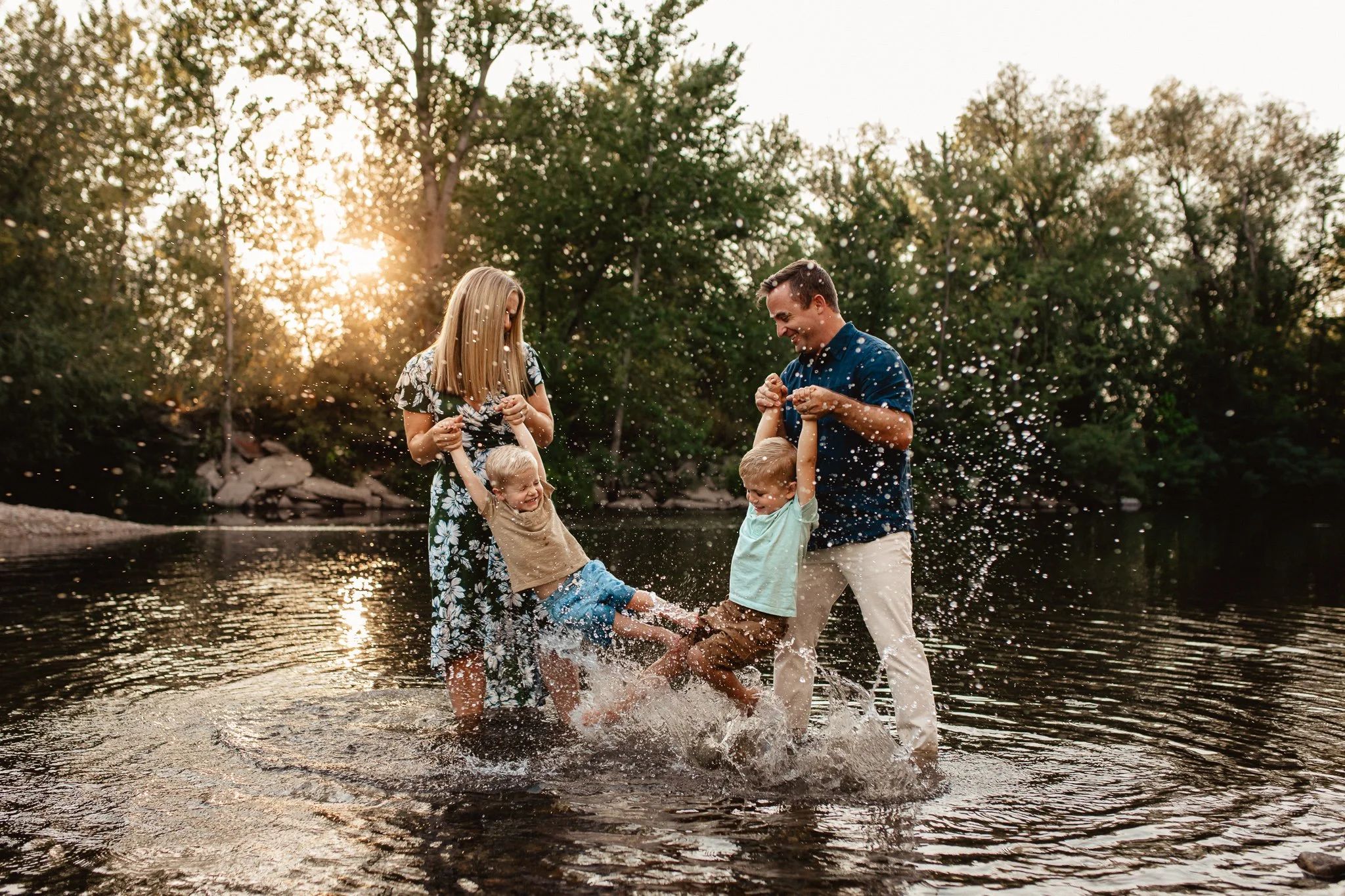 Parents holding their boys who are splashing in the river water at sunset