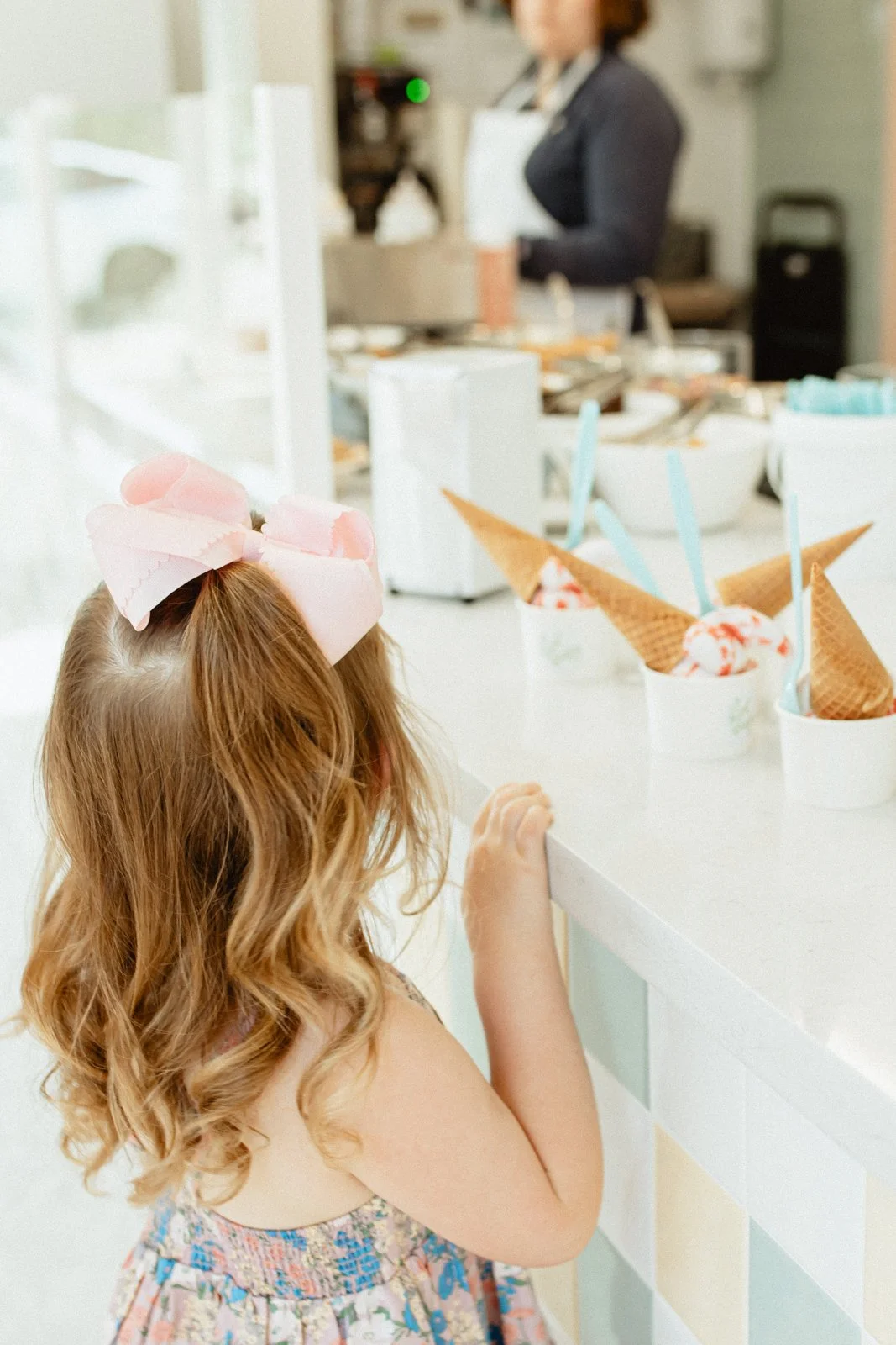 Little girl peeking over ice cream counter at ice cream cones