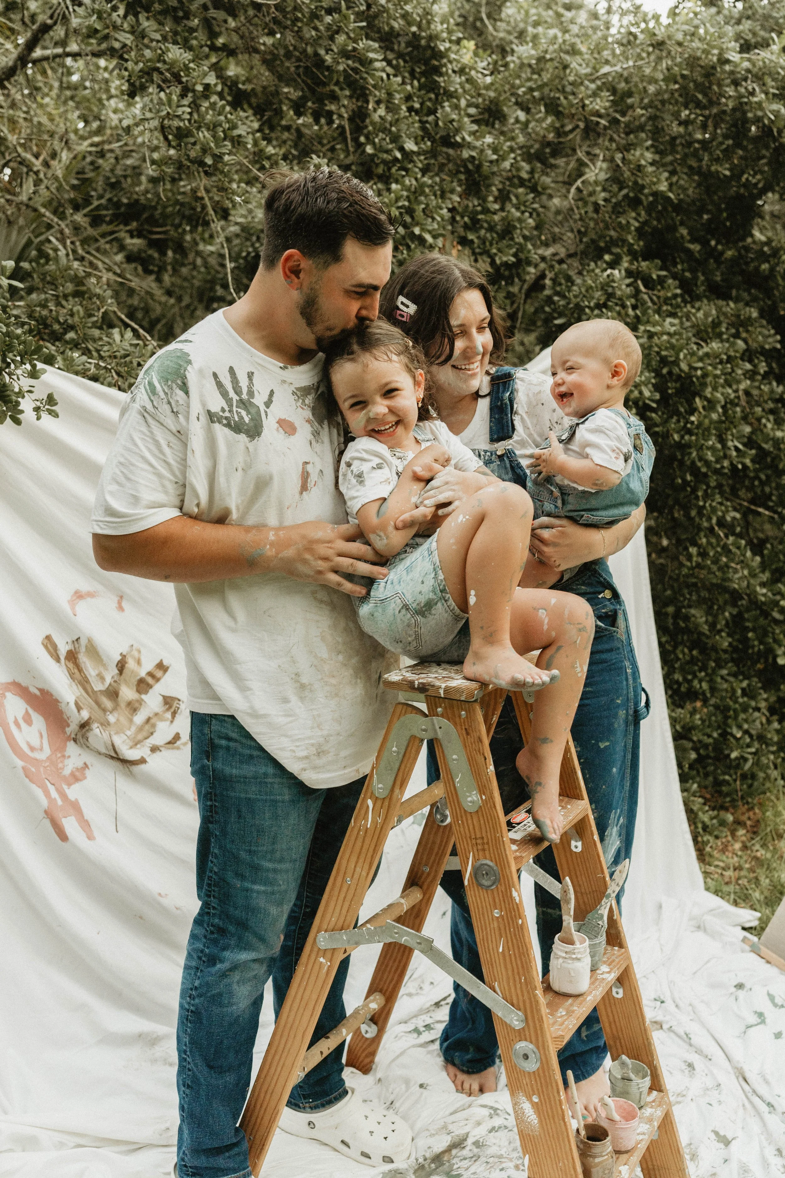 Family of four posed with little girl on ladder and paint all over them